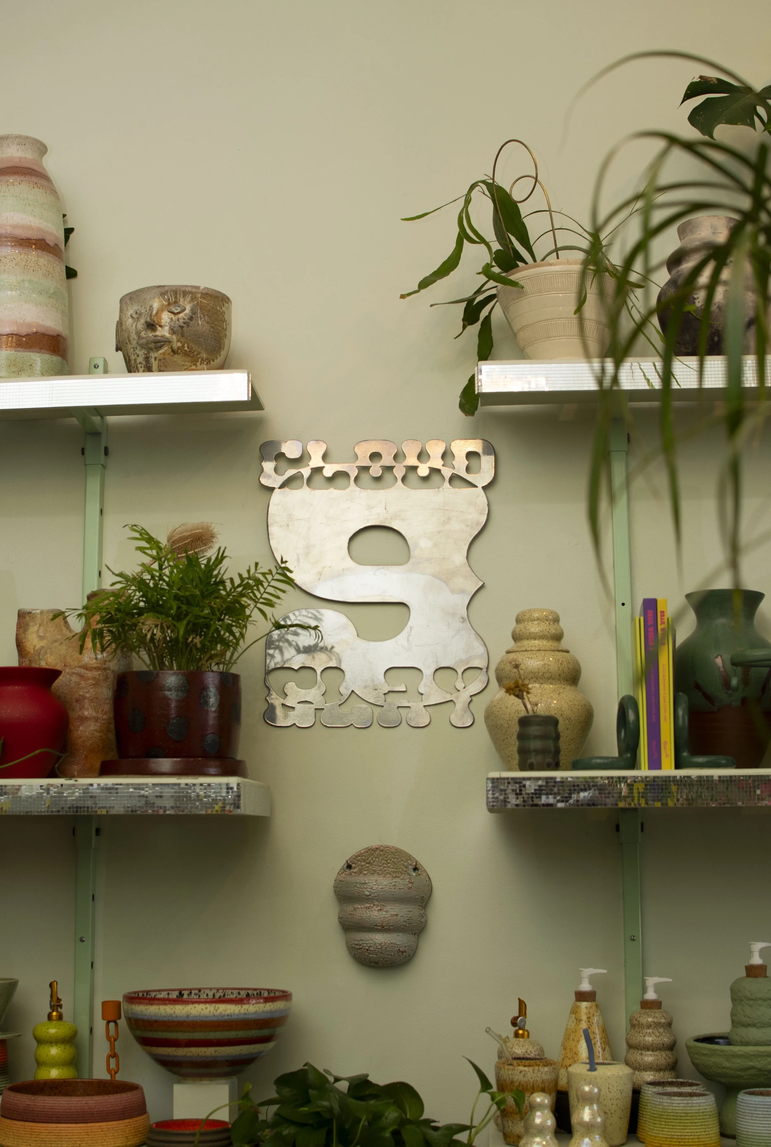 Display of pottery and decorative items on shelving units, with the word 'CLOUD 9 CLAY' on the wall behind.
