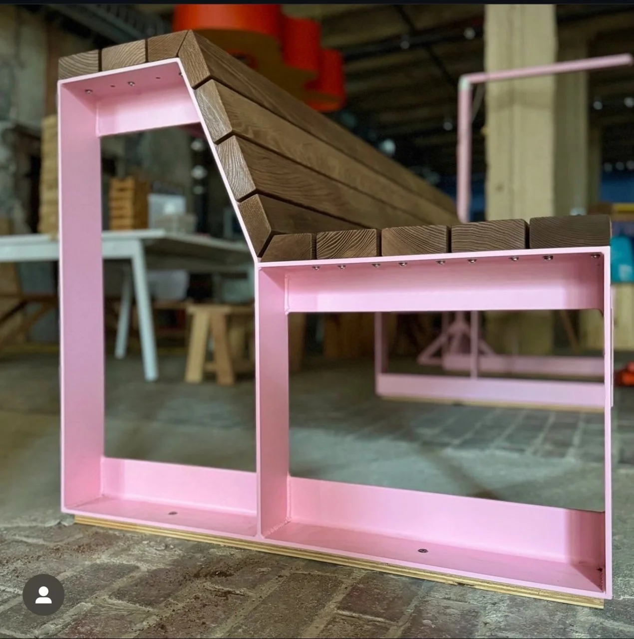 A modern bench with a wooden slat seat and pink metal frame in a workshop.