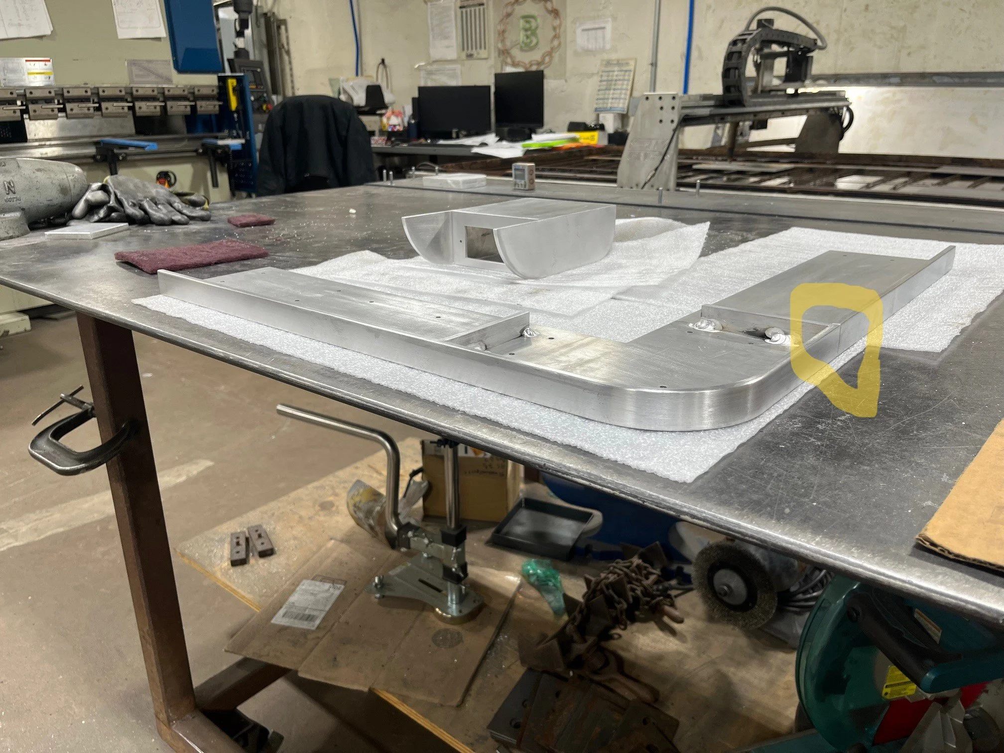 Metal work table in a workshop with aluminum parts, tools, and foam padding.