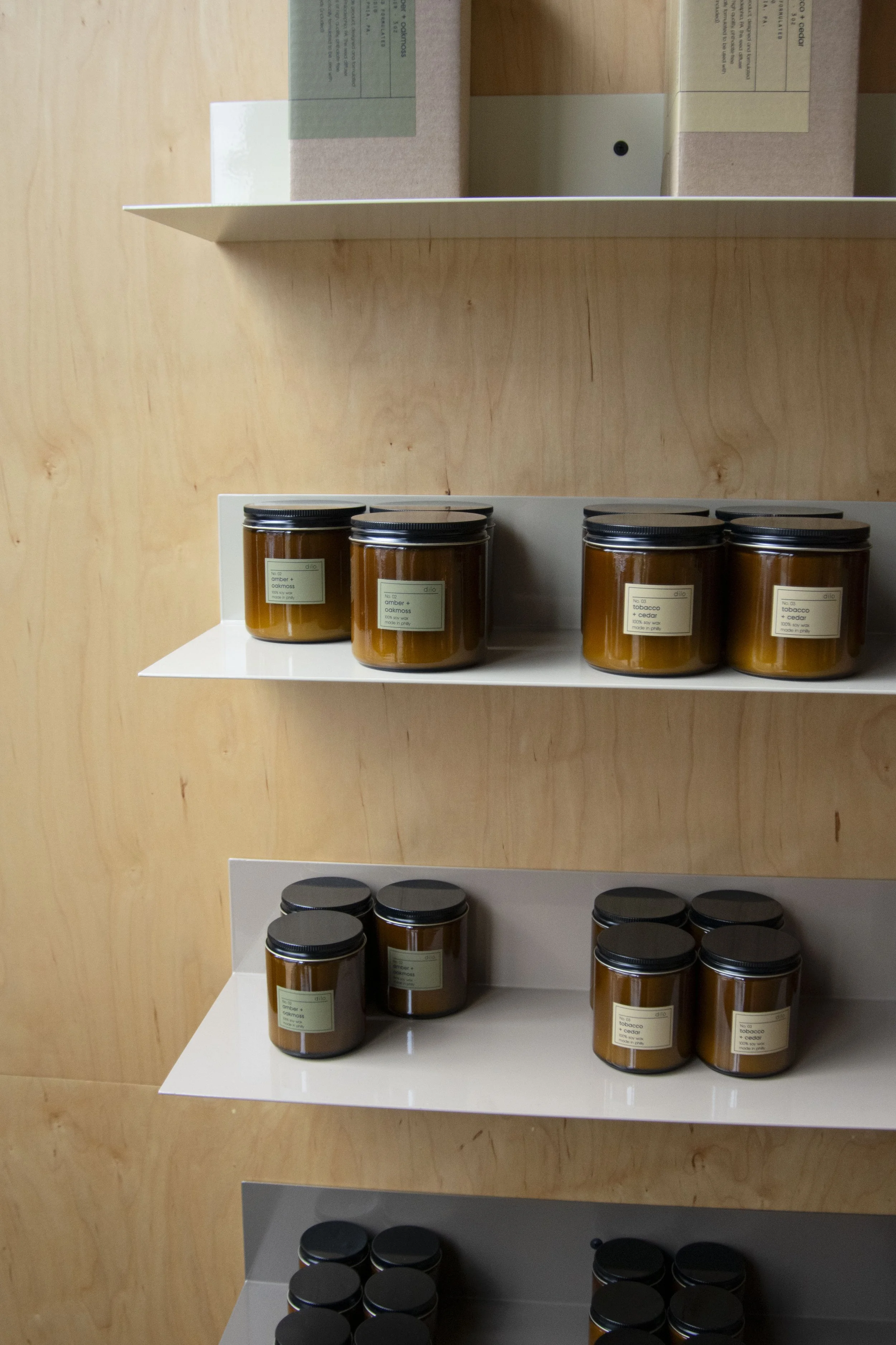 Bent steel shelving holding candles, mounted to plywood walls. Each shelf is a varying shade of beige, creating an overall ombre effect.