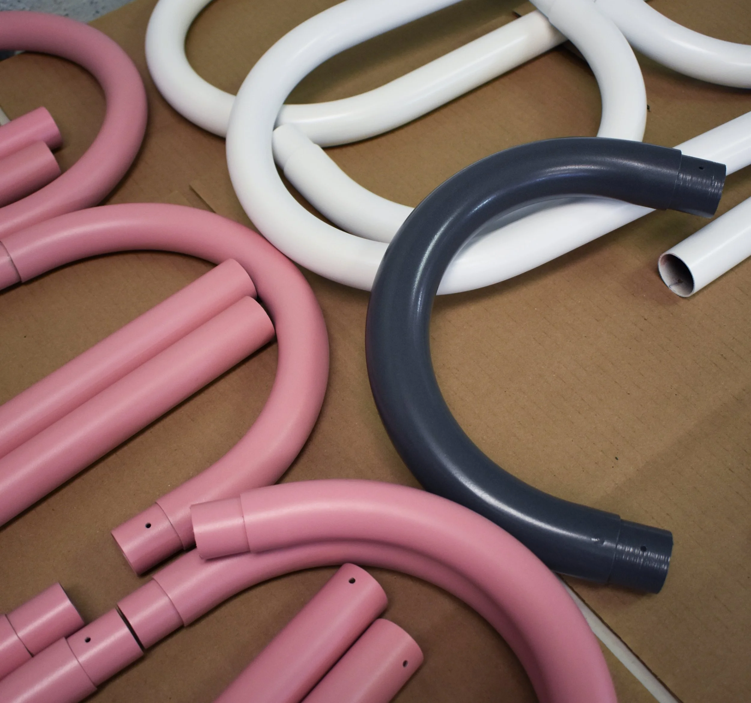 Multiple flexible tubes or hoses in pink, white, gray, and off-white colors, arranged on a brown surface.