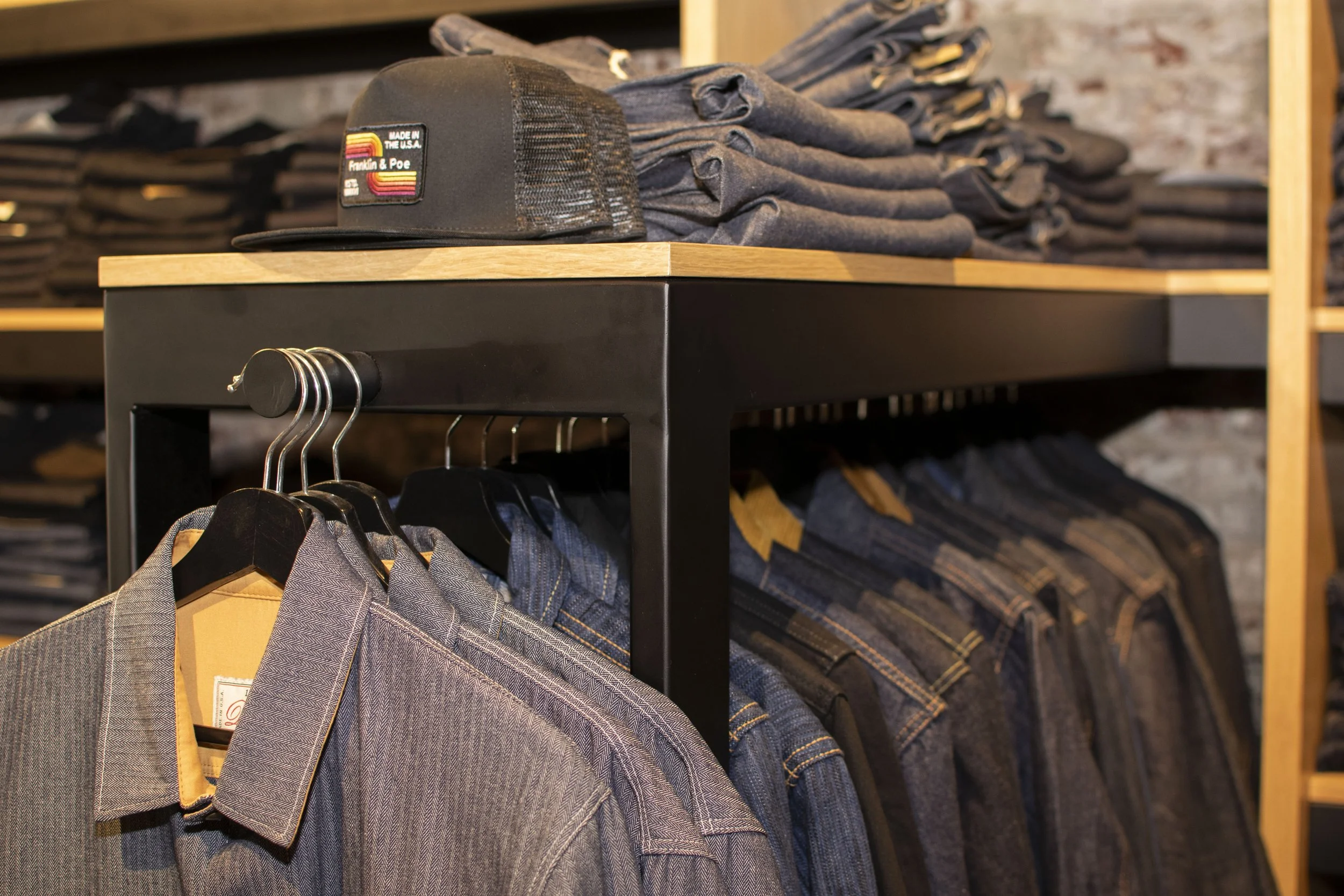 Overall view of inside Franklin and Poe clothing store with steel and wood displays holding folded mens shirts, boots and denim. 