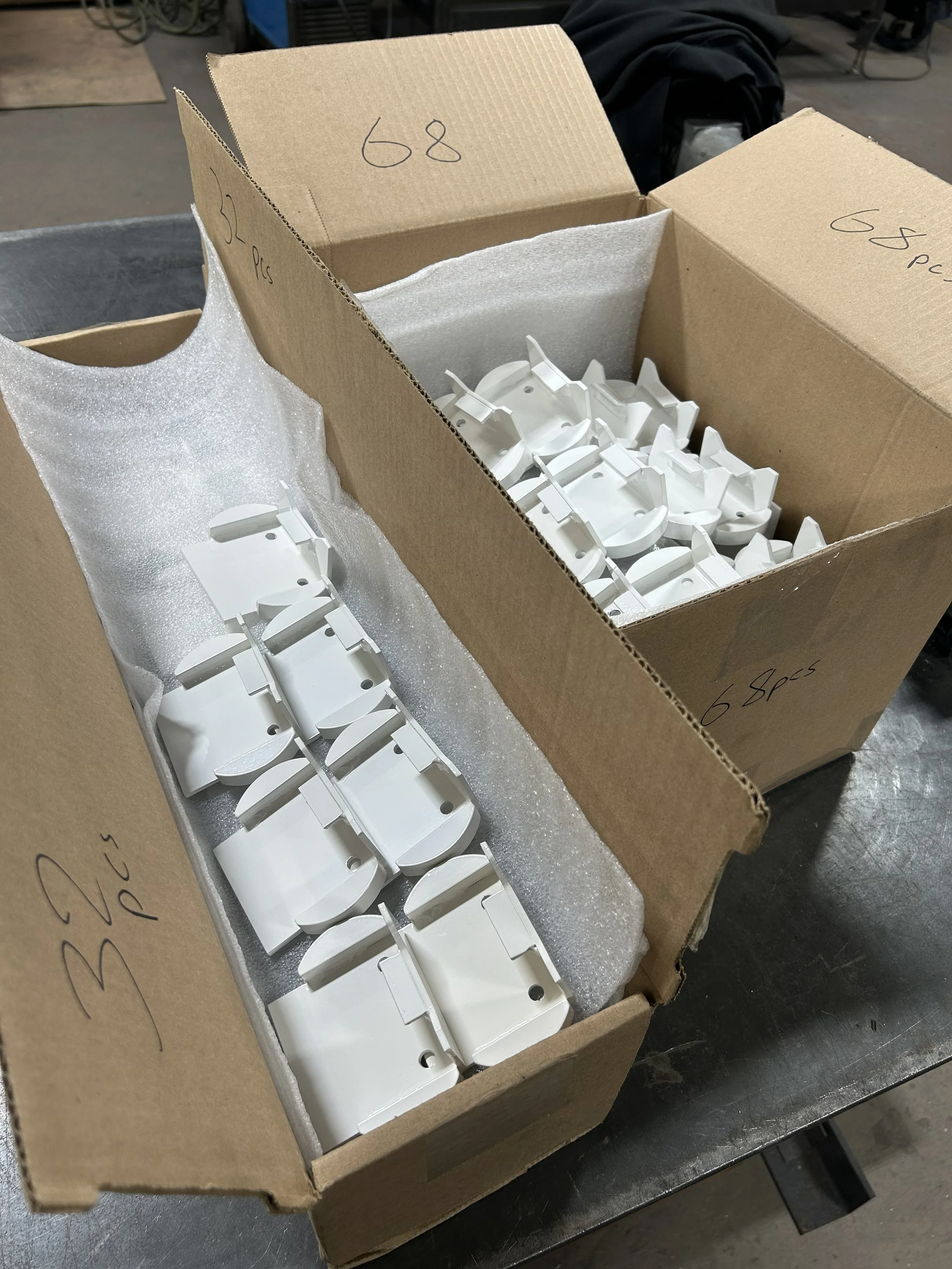 Open cardboard box containing white powder coated steel brackets.