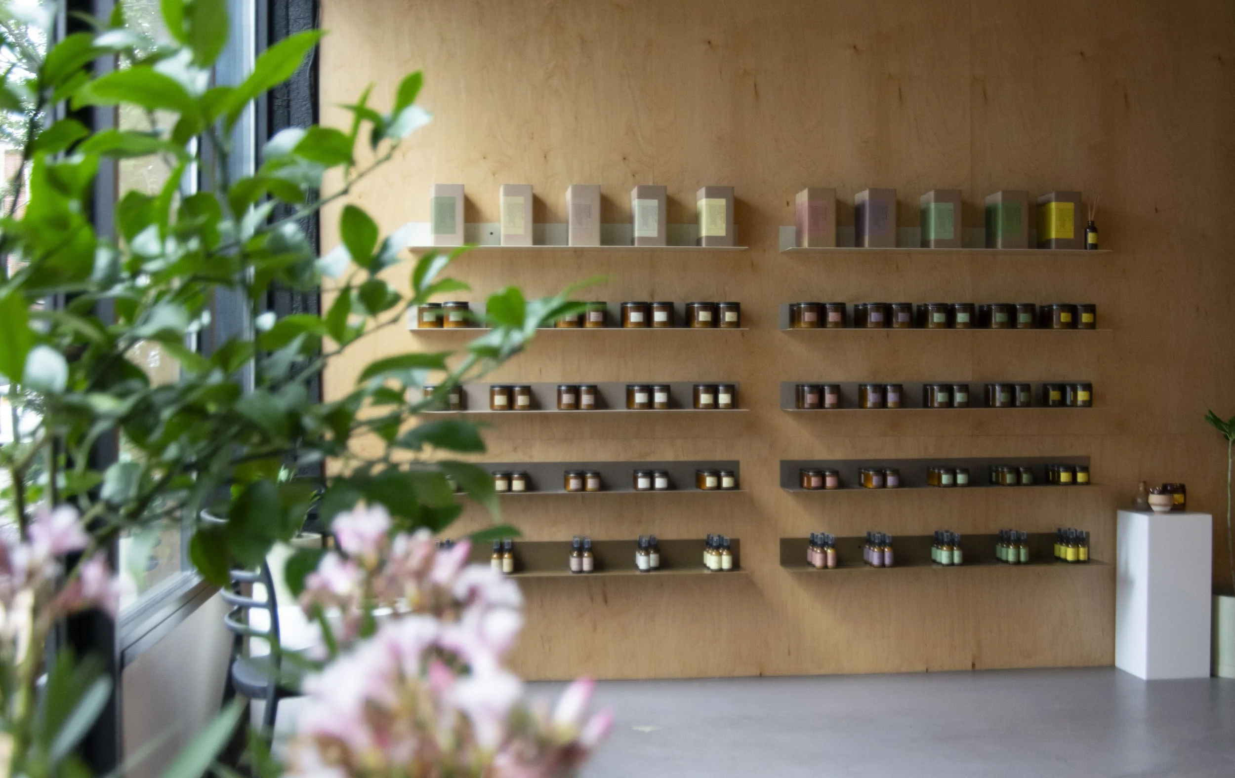 Bent steel shelving holding candles, mounted to plywood walls. Each shelf is a varying shade of beige, creating an overall ombre effect.