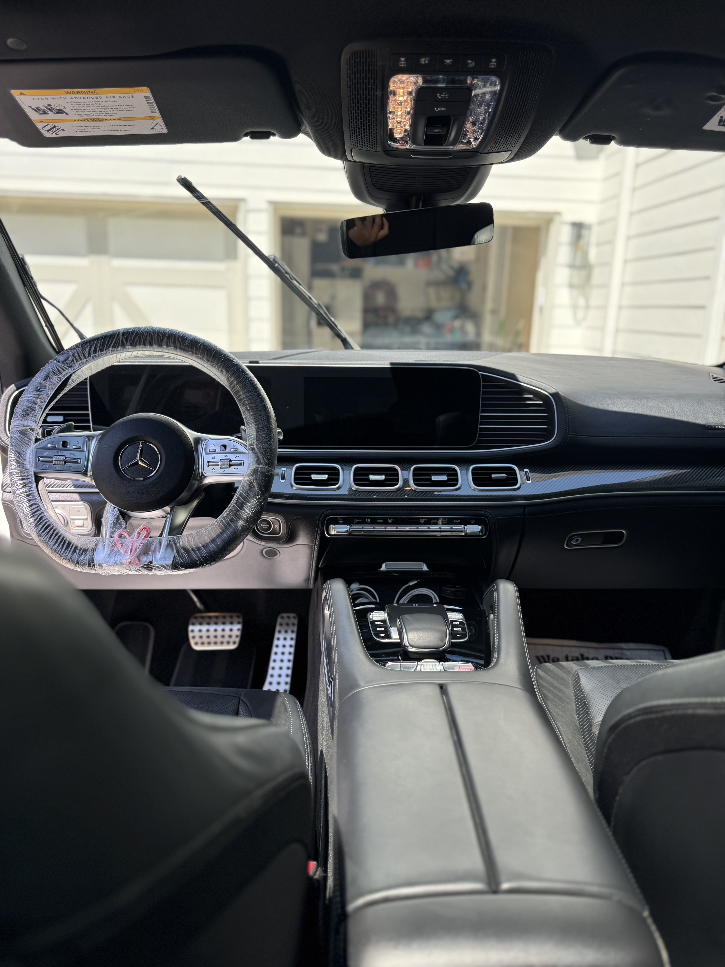 Interior of a luxury Mercedes-Benz vehicle, showing the dashboard, steering wheel with Mercedes logo, gear shifter, and front seats. The dashboard has a large central display and air vents, with metallic accents.