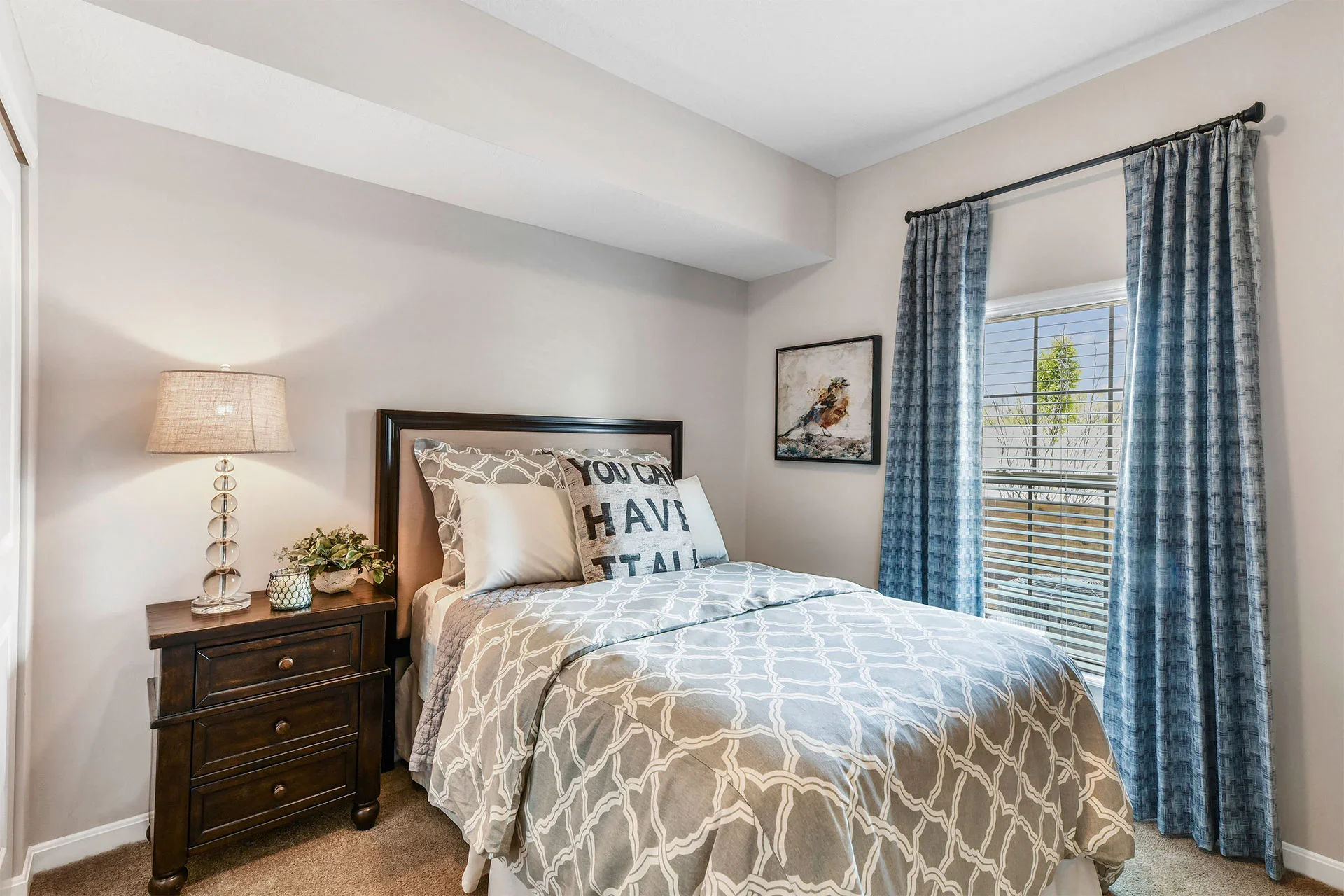 A bedroom with a bed, nightstand, and window with blue curtains.