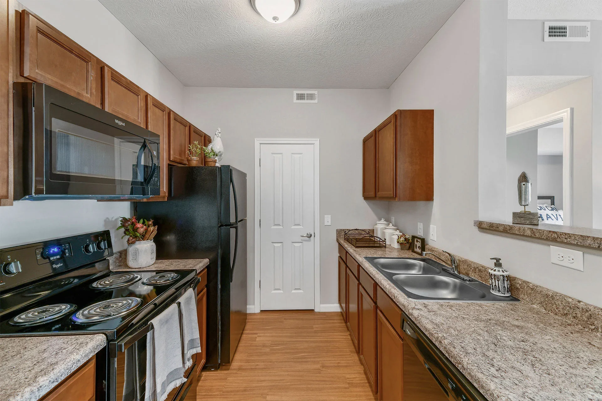 Kitchen with wooden cabinets, stove, black refrigerator, granite countertops, dual sink, and decor items on the counter and upper shelves.