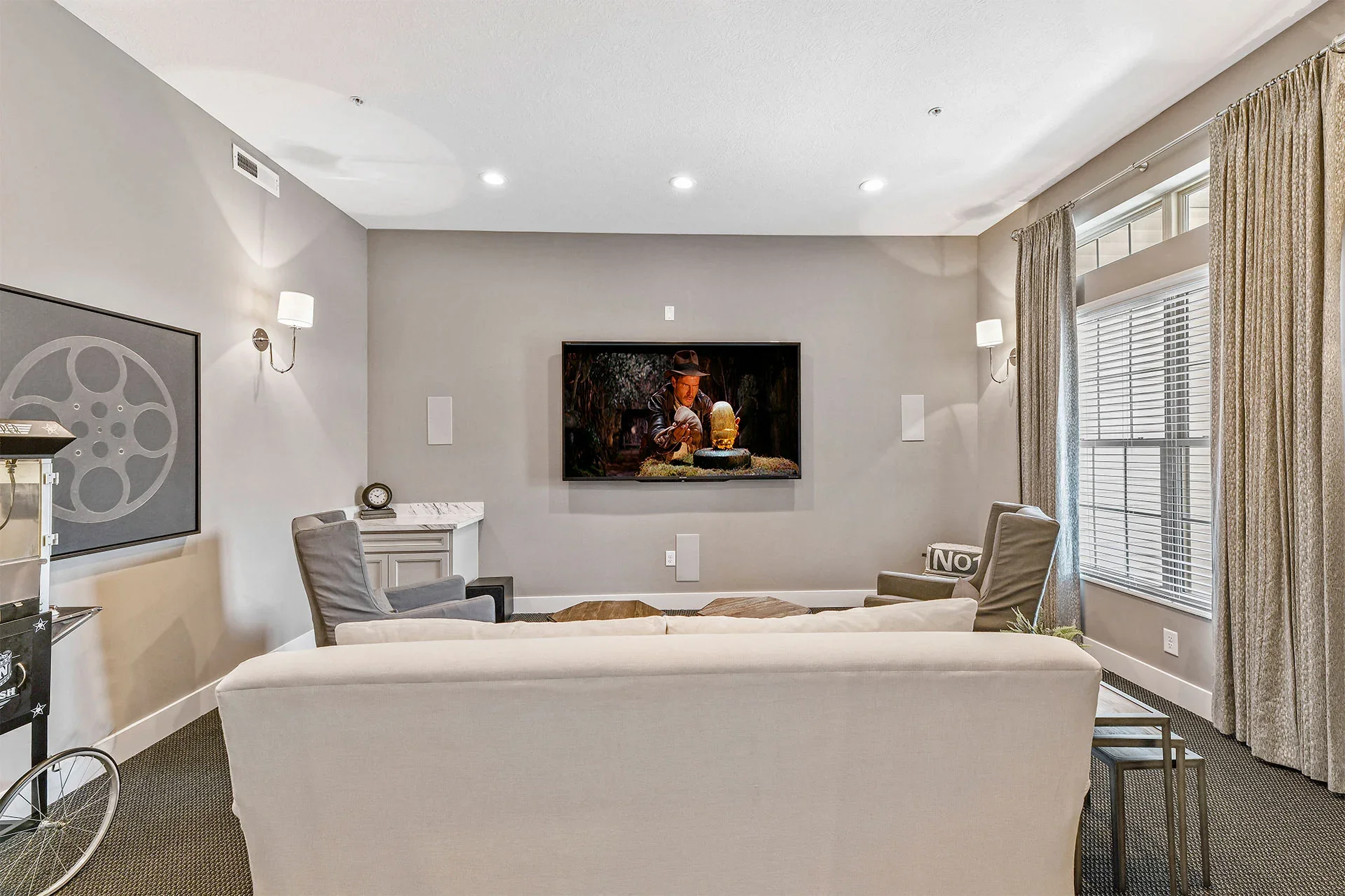 Living room with gray walls, beige curtains, large windows, white sofa, gray chairs, wall-mounted TV, and decorative items.