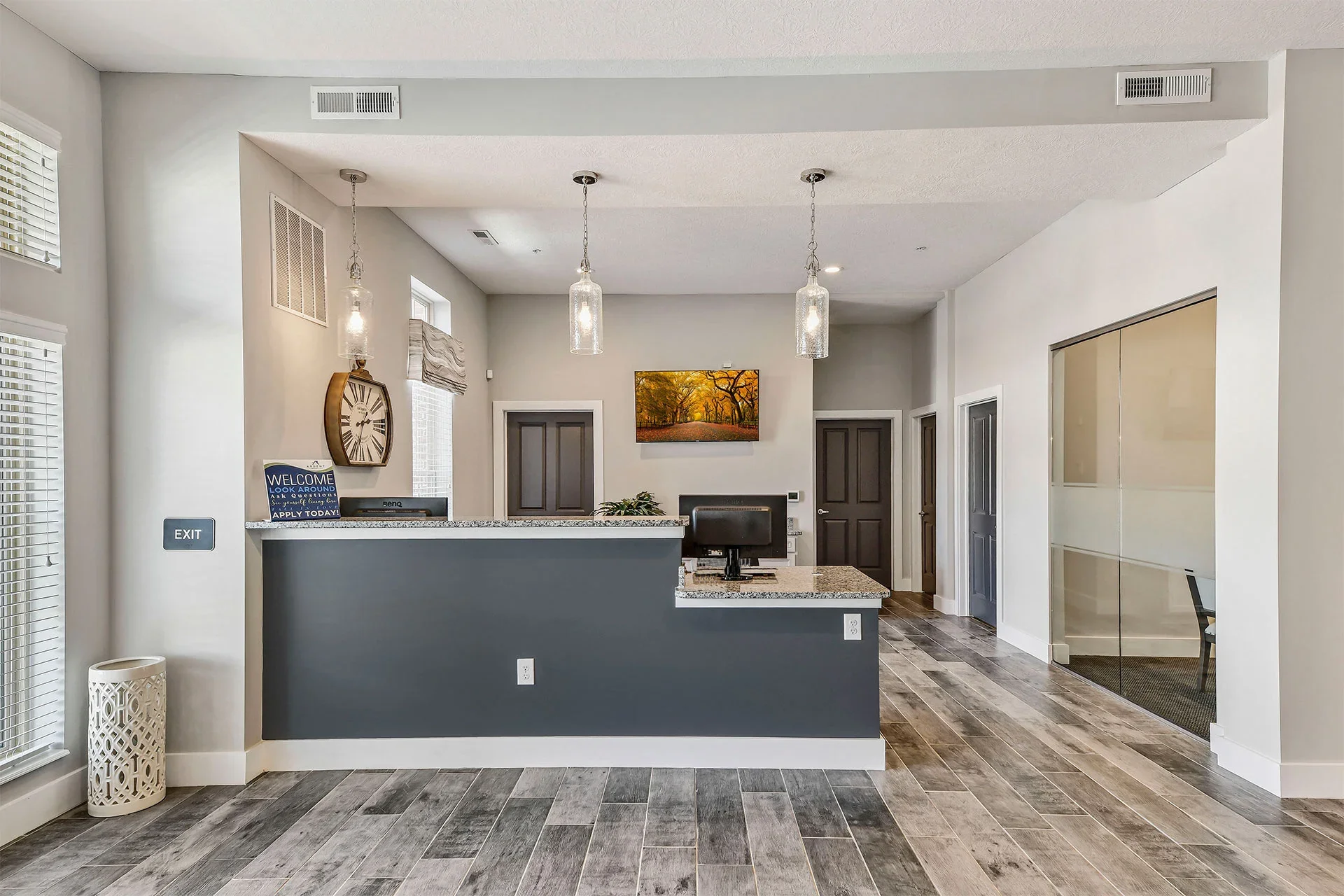 Interior view of a modern reception area with a gray and white color scheme, pendant lights, a digital monitor, and artwork on the walls.
