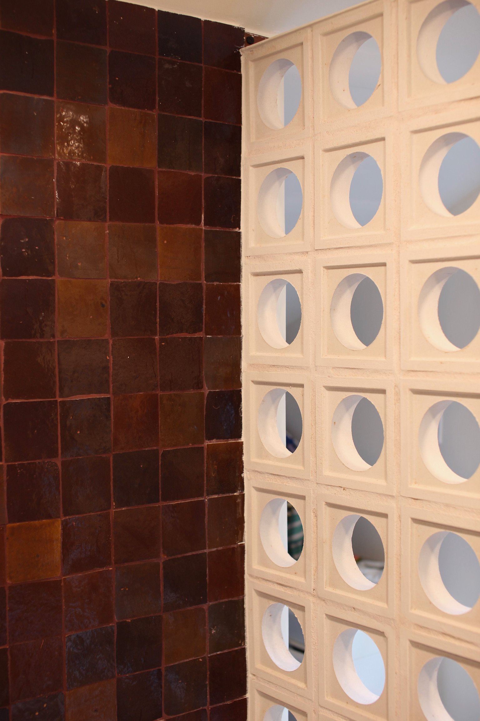 Close-up of a wall with dark red glossy ceramic tiles on the left and a white section with circular holes on the right, possibly part of a decorative or functional partition.