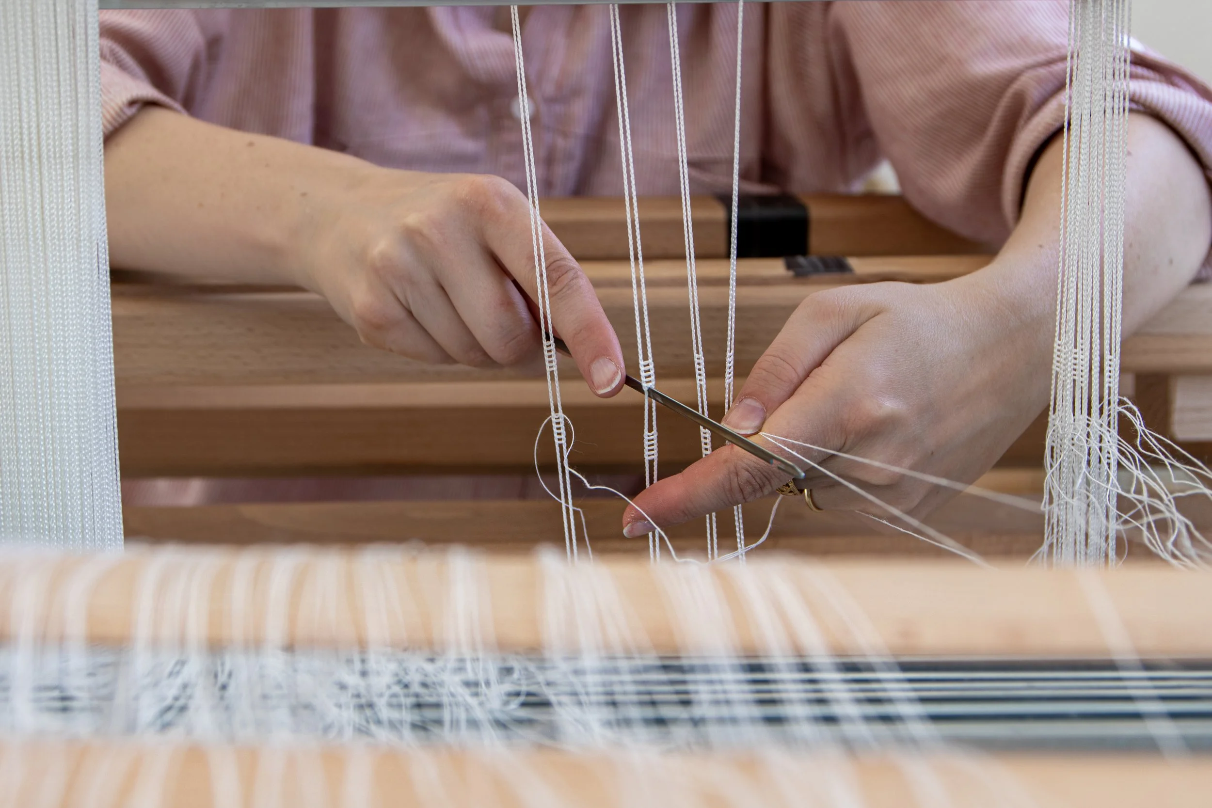 Une personne use des outils pour tisser ou réparer un métier à tisser en bois avec des fils blancs.