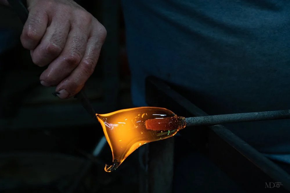 Un artisan en train de souffler du verre molten pour créer un objet en verre chaud dans un atelier de verrerie.