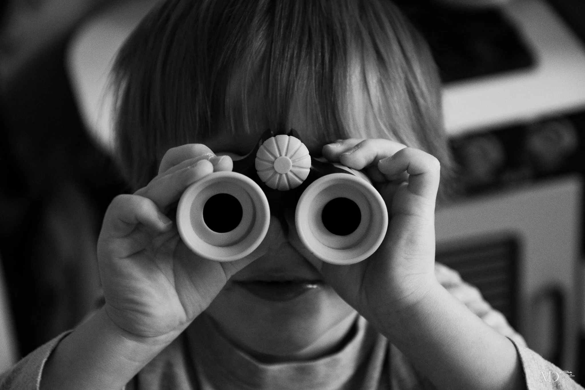 Enfant regardant à travers une paire de jumelles, vue de dos, en noir et blanc.