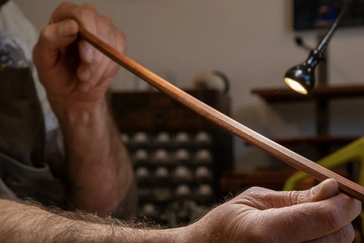 Une personne tient une longue baguette en bois, probablement utilisée pour jouer d'un instrument à cordes ou à vent.