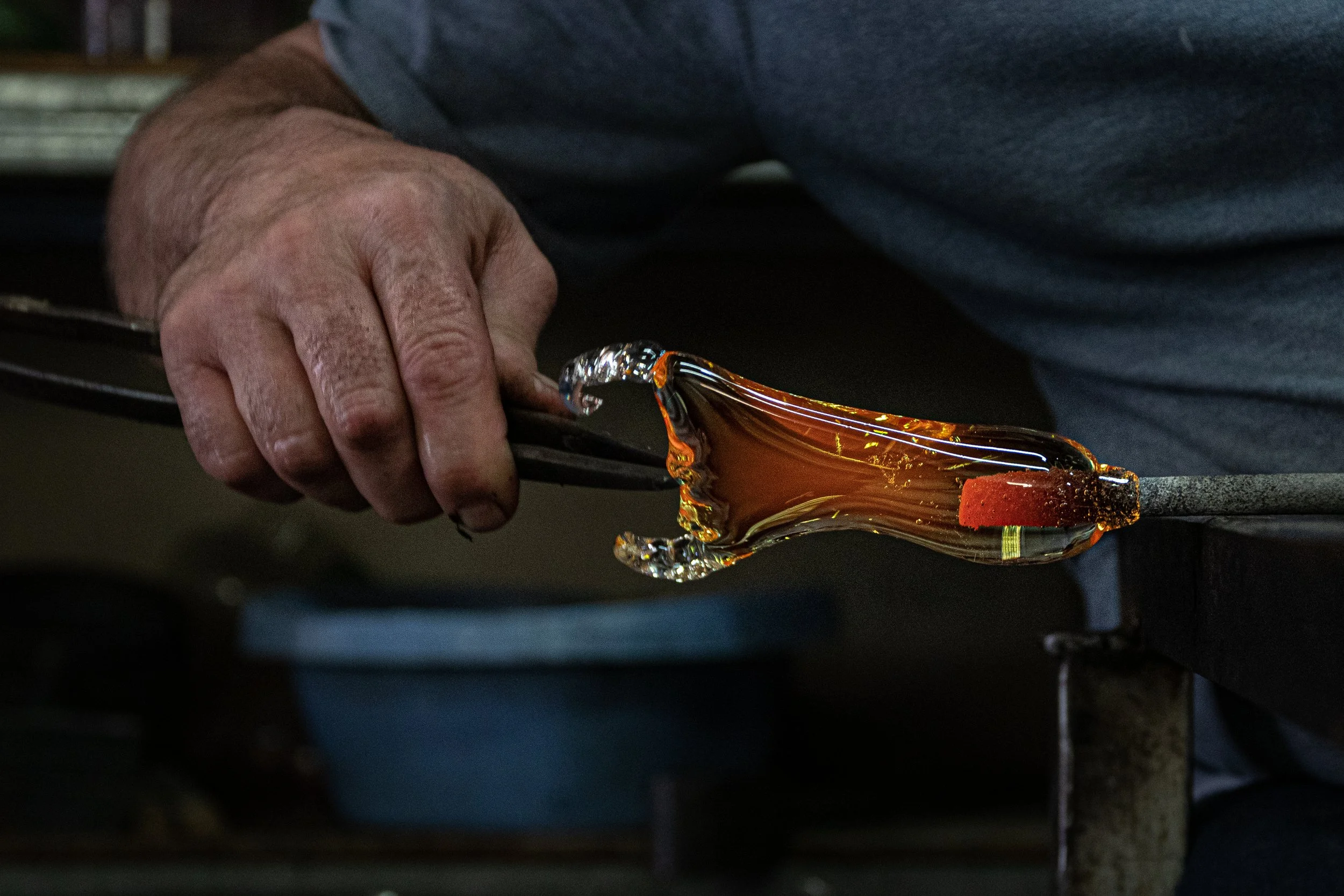Un artisan soufflant du verre rouge chaud pour créer une pièce en verre.