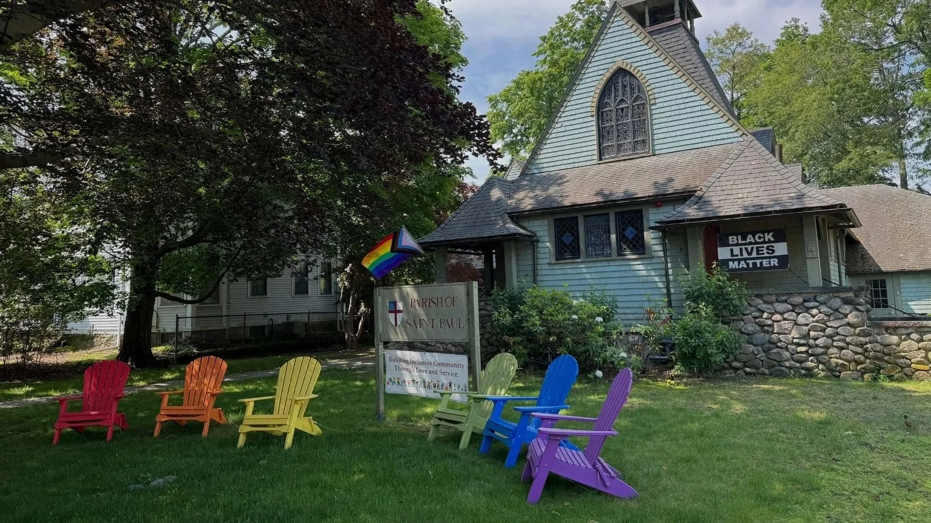 Parish of St. Paul lawn with rainbow adirondack chairs, pride flag, "black lives matter" sign, and the exterior of the church