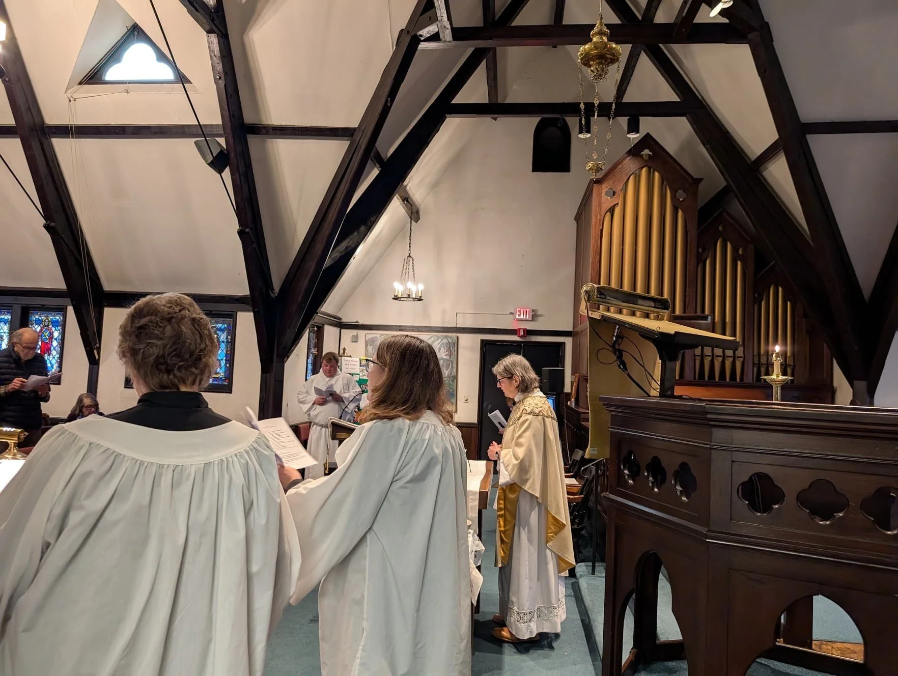 The choir sings during a church service inside Parish of St. Paul, with stained glass windows, dark wood beams, an organ, and a candle on the pulpit.