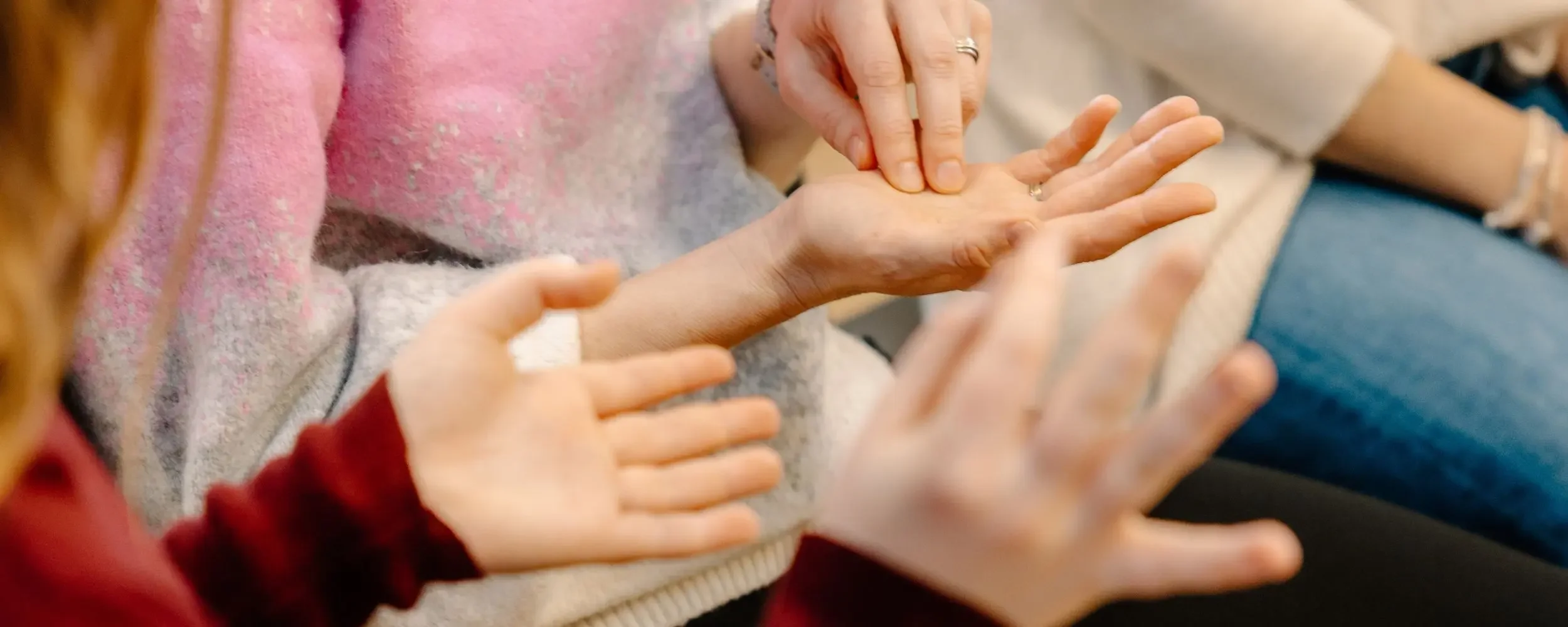 Zwei Menschen, die Hände berühren, in einer Näheaufnahme. Eine Person legt ihre Hand auf die Hand einer anderen Person, während eine weitere Person mit einer Hand die andere berührt. Es ist eine Szene mit mehreren Händen, die Interaktion und Nähe anzeigen.