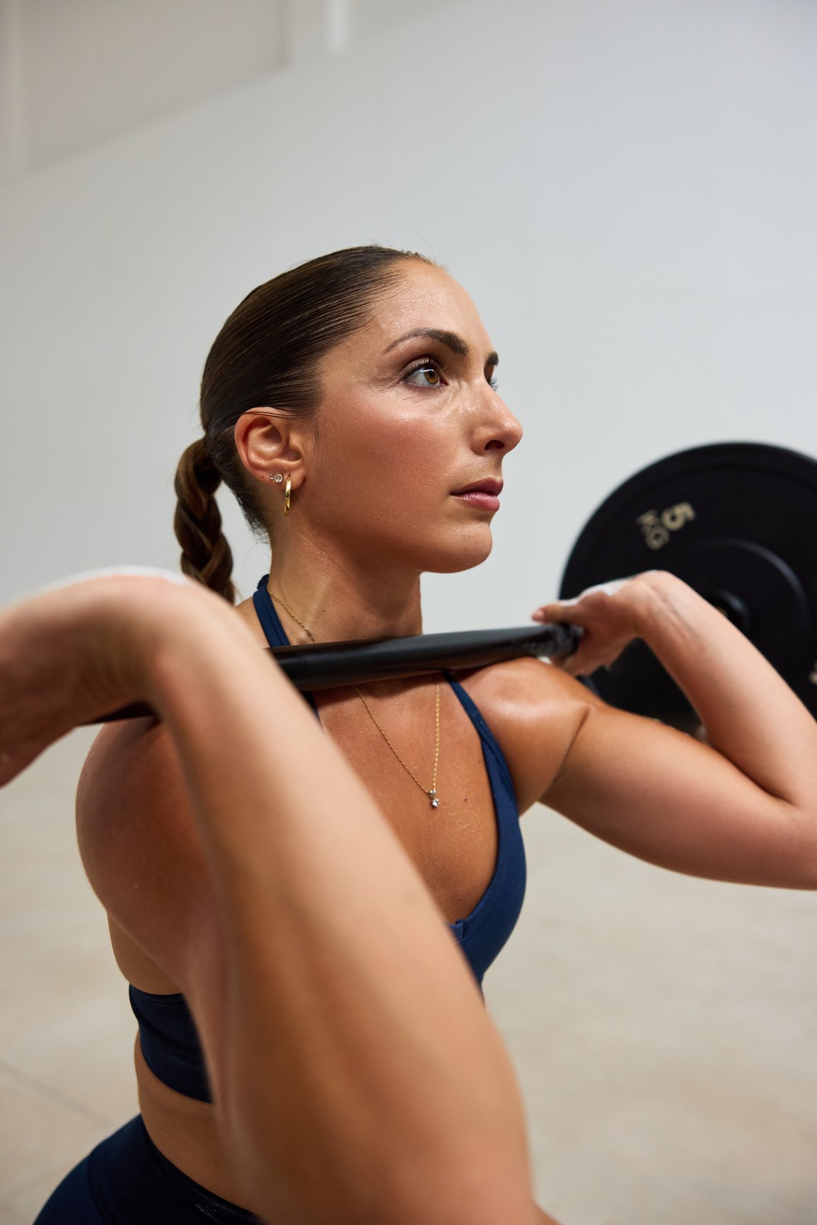 Ridge Haven - New Townhomes for Rent in Concord | A woman with dark brown hair in a braid performing a squat exercise with a barbell on her shoulders in a gym.
