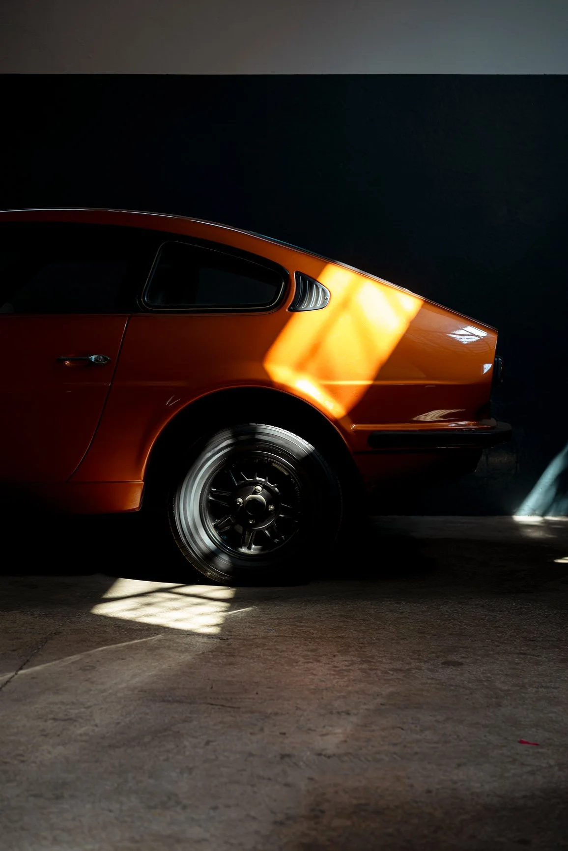 Ridge Haven - New Townhomes for Rent in Concord | A partial side view of a vintage orange car with black wheels, illuminated by sunlight in a dark indoor setting.