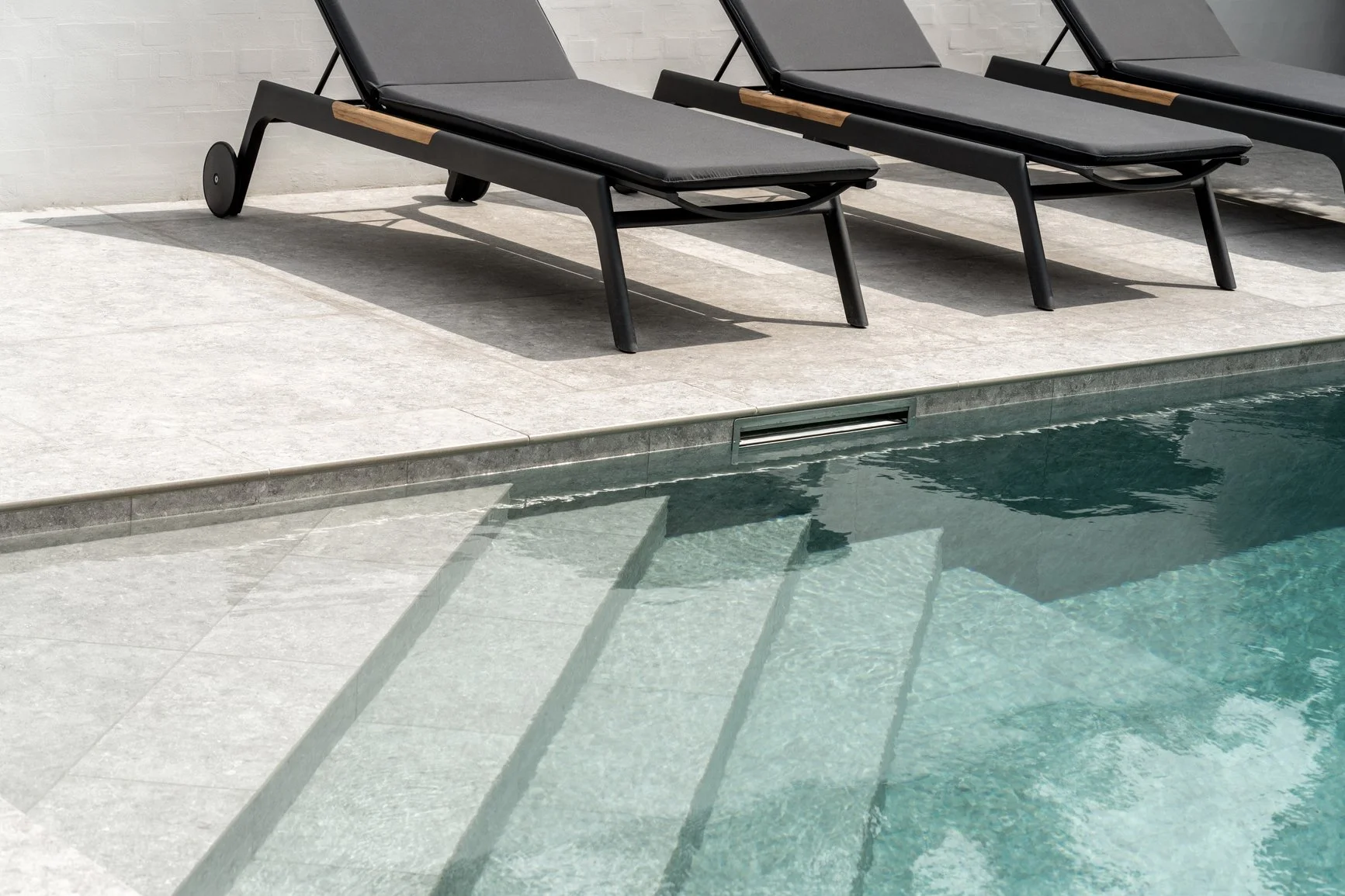 Ridge Haven - New Townhomes for Rent in Concord | A row of black outdoor lounge chairs with gray cushions next to a swimming pool.