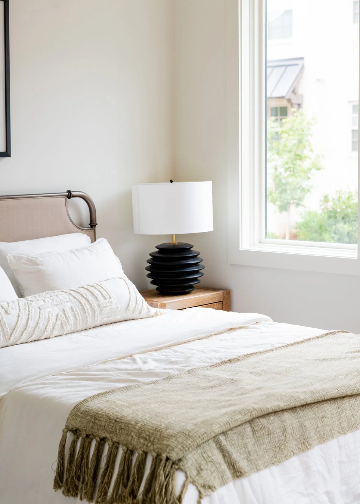 Ridge Haven - New Townhomes for Rent in Concord | A bedroom with a bed, multiple pillows, a bedside table, and a black table lamp. There is a large window with a view of trees and building outside.