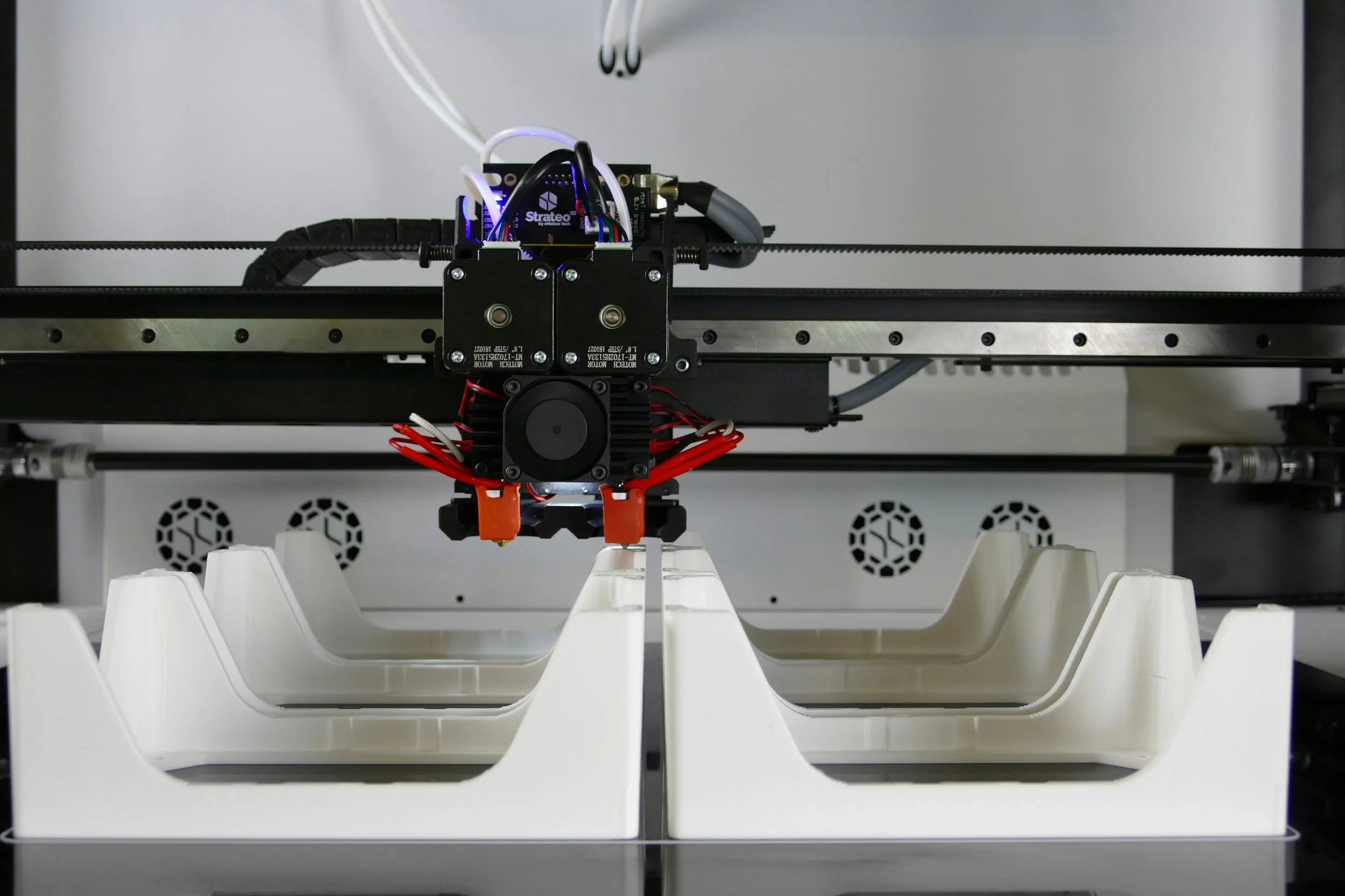 Close-up of a 3D printer extruder assembly printing over a white plastic used as support material.