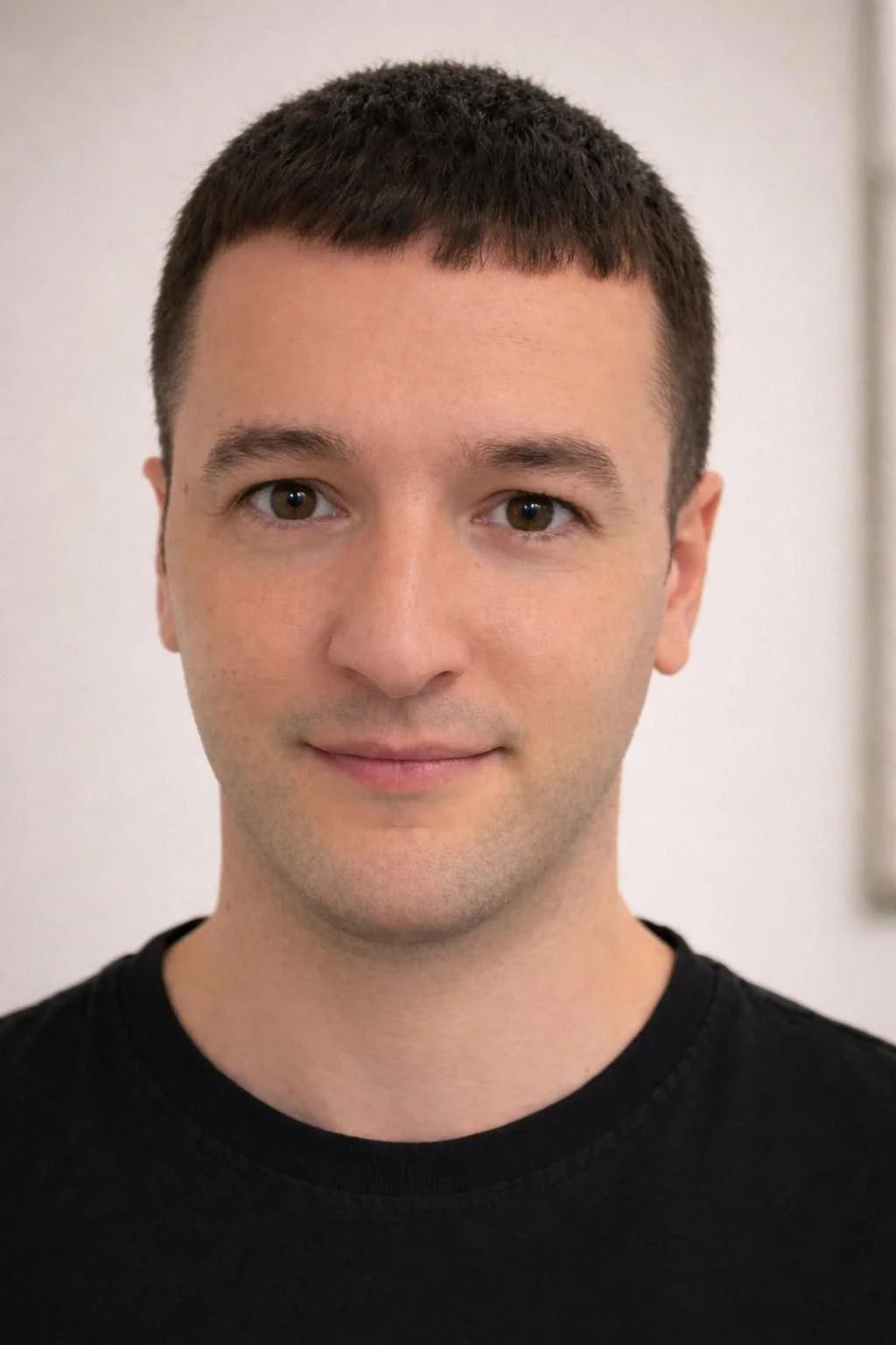 Retrato de un hombre joven con cabello corto y piel clara, sonriendo ligeramente, vestimenta negra.