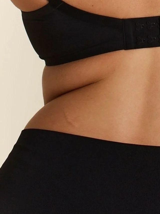 Parte del torso de una persona con piel medianamente tonificada, usando ropa negra ajustada, en un fondo claro y liso.
