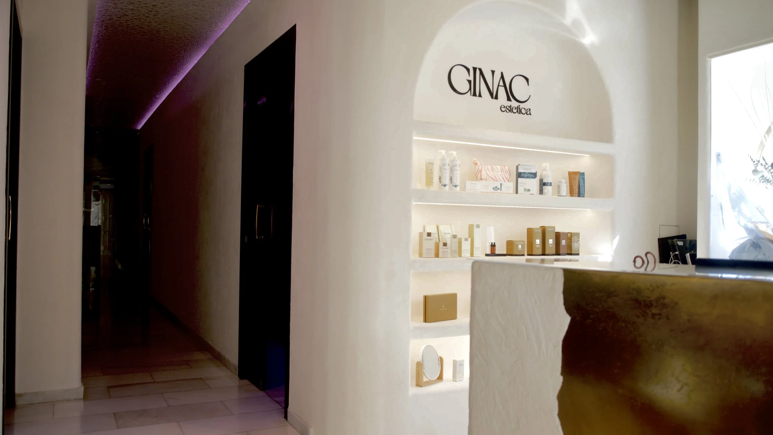Mostrador de una clínica estética con productos de cuidado facial en estanterías iluminadas, señal que dice 'GINAC estética'.