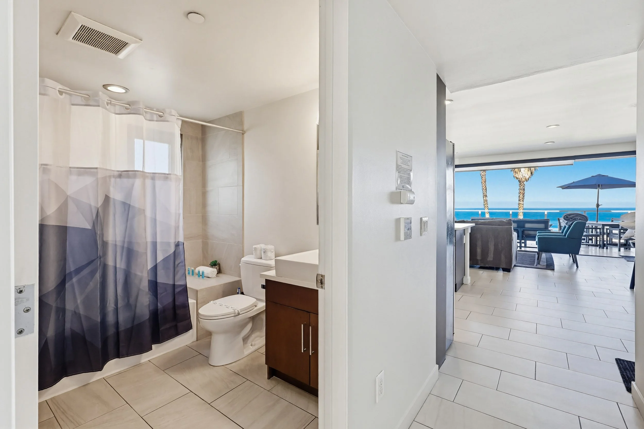 Bathroom with shower curtain, toilet, vanity, and view of patio with outdoor furniture and ocean view