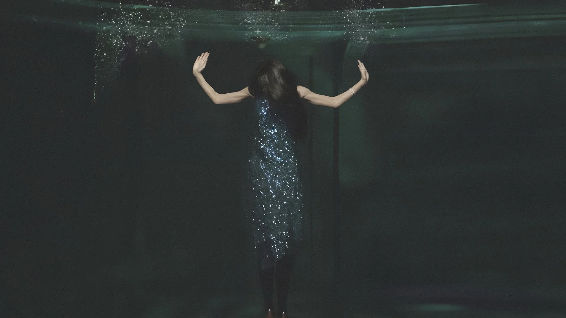 A woman in a sparkly dress is underwater with her arms outstretched and her hair floating around her.