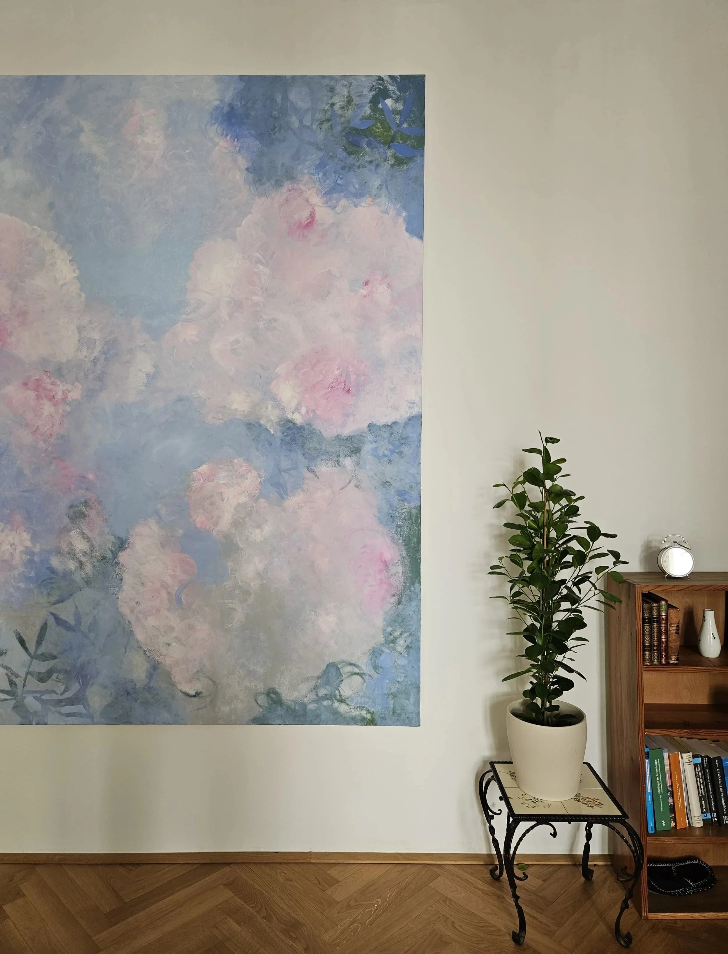 Eine Praxis für Personzentrierte Psychotherapie mit einem großen, abstrakten Wandbild in Pastellfarben, einem hohen grünen Topfpflanze auf einem dekorativen Beistelltisch und einem Bücherregal.