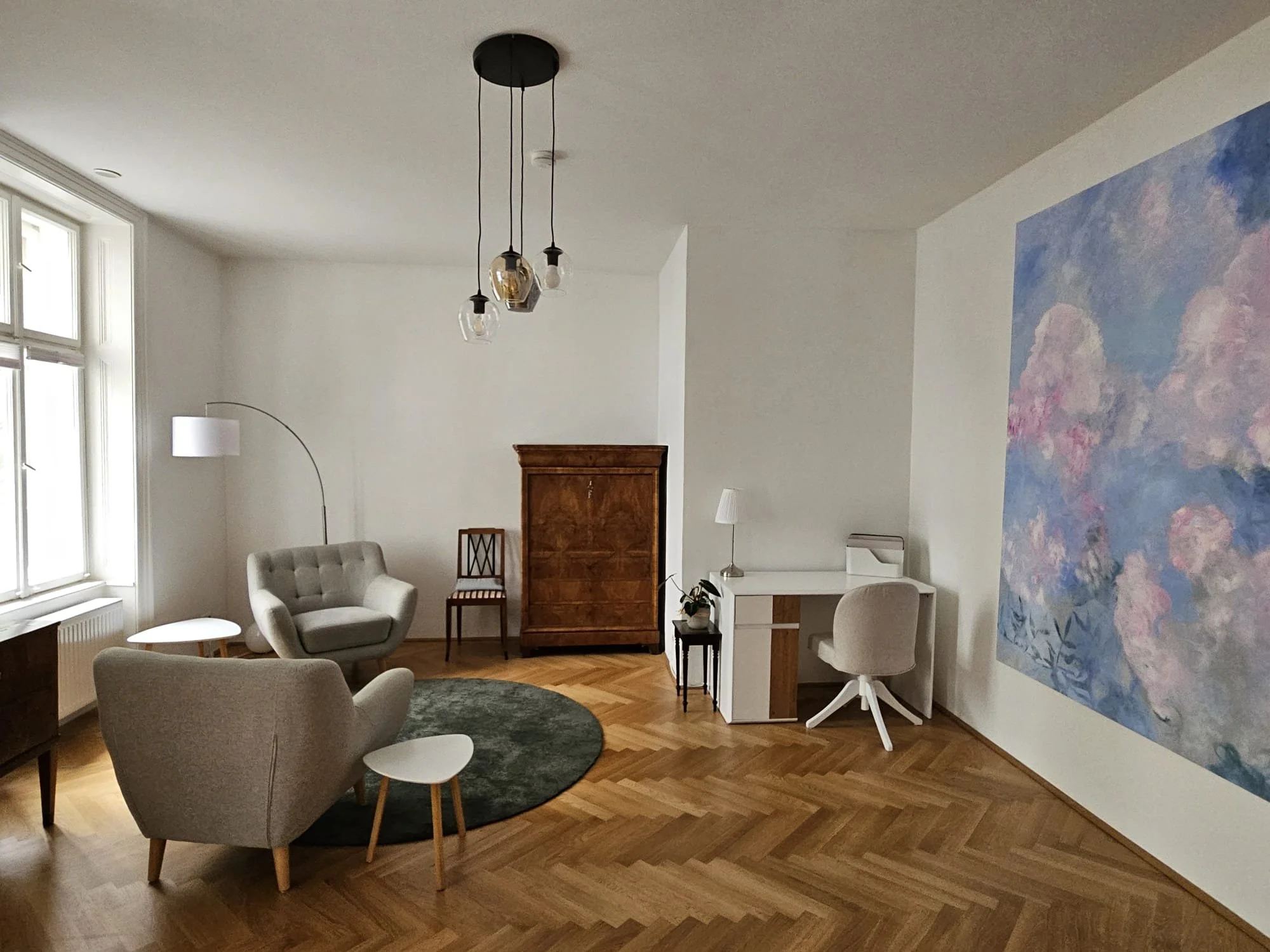 Moderne Praxis für Personzentrierte Psychotherapie in Wien mit großen Fenstern, zwei weißen Sesseln, einem kleinen weißen Tisch, einer dunklen Teppich, einem antiken Holzmöbel, einem weißen Stuhl, einem großen Wandbild.