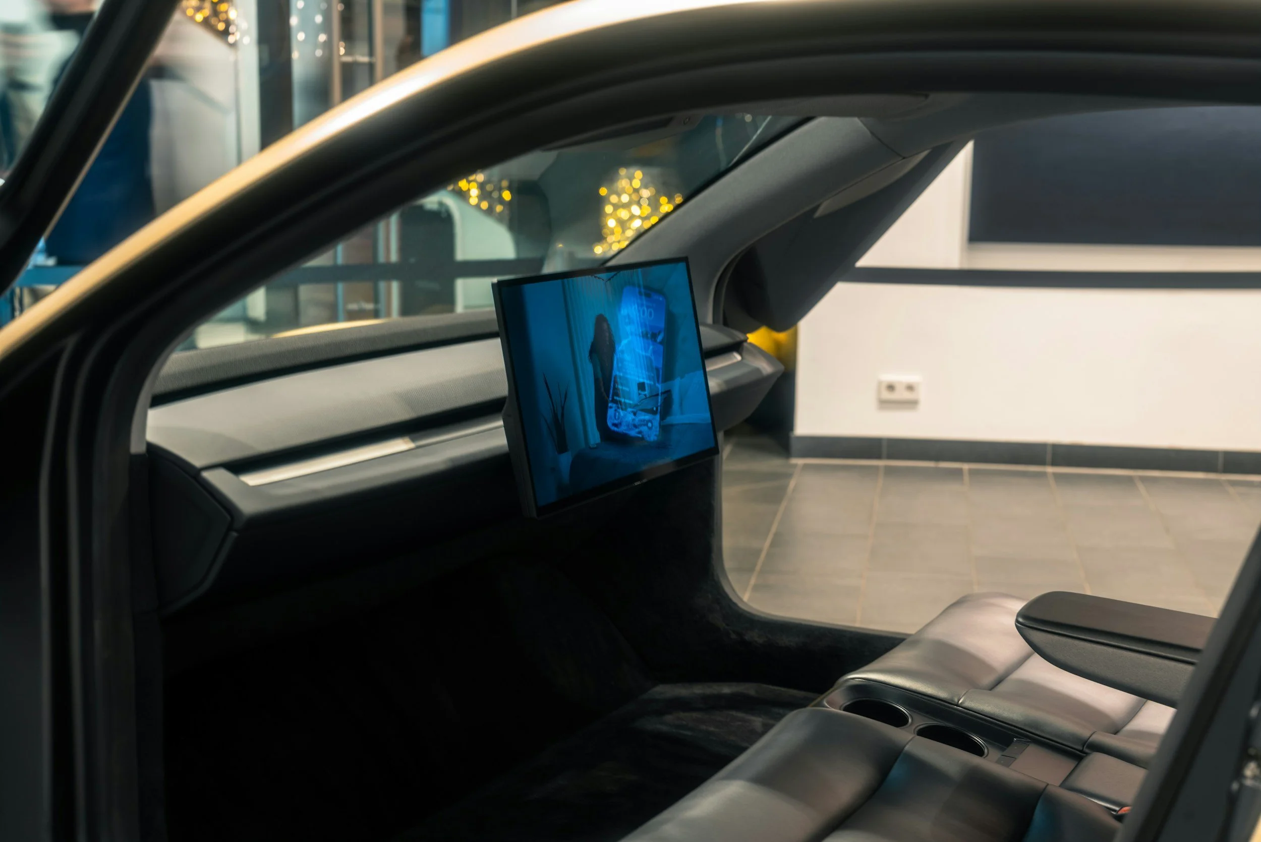 Inside a modern car, showing the dashboard with a screen and a view through the window to a building with holiday lights.