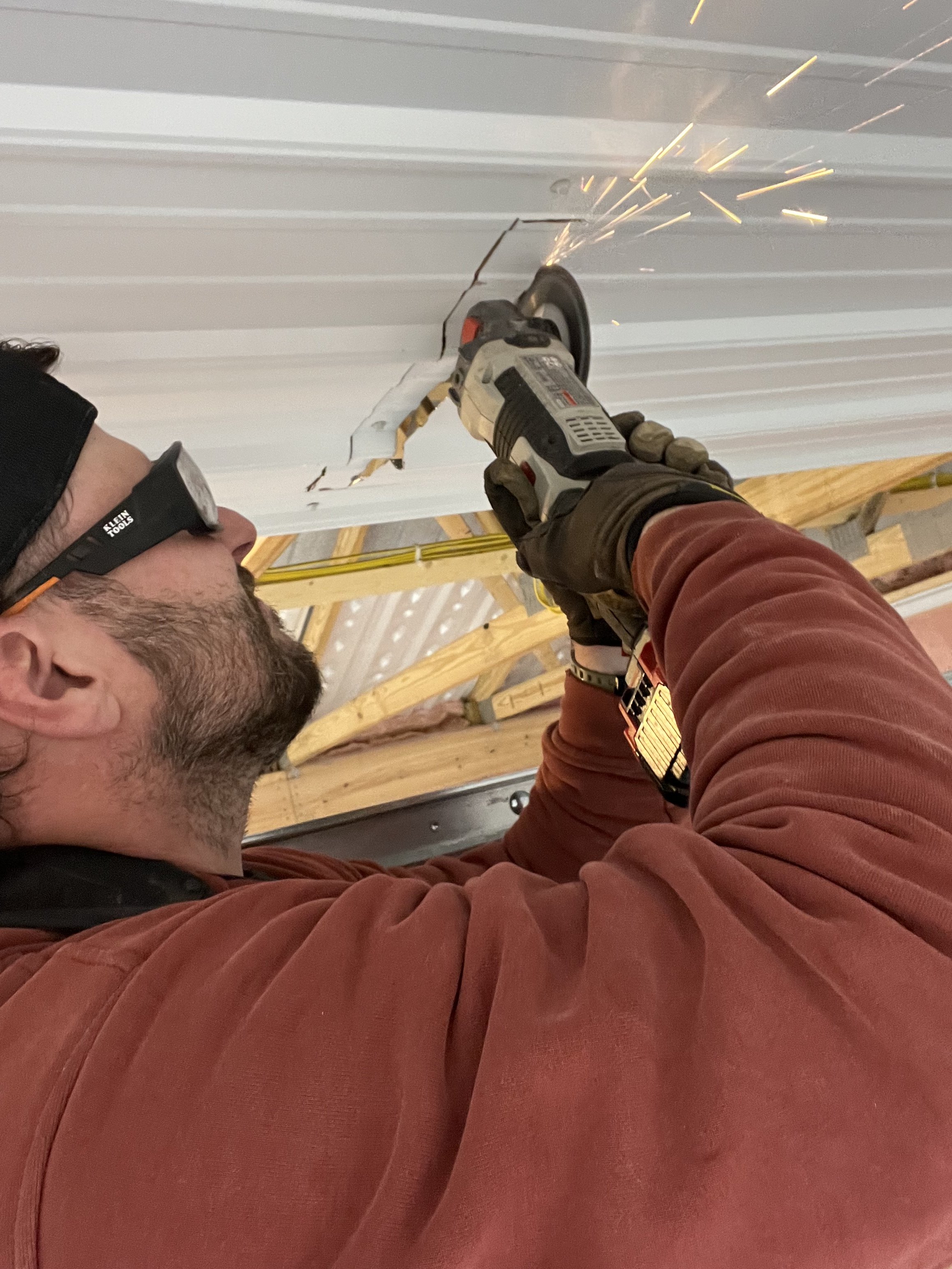 A man wearing safety glasses using an angle grinder to cut through a piece of metal, creating sparks in an indoor construction or workshop setting.