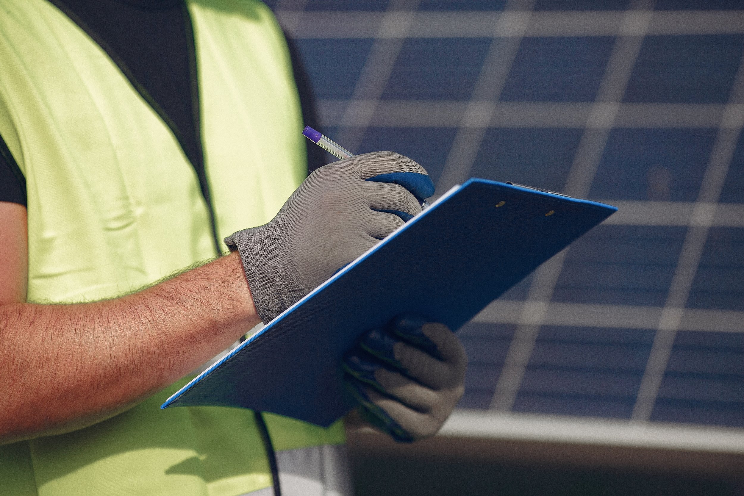 A person in a yellow safety vest and gray glove holding a writing pad and a pen.