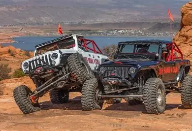 Two off-road Jeeps parked on a rocky landscape with a body of water and mountains in the background.