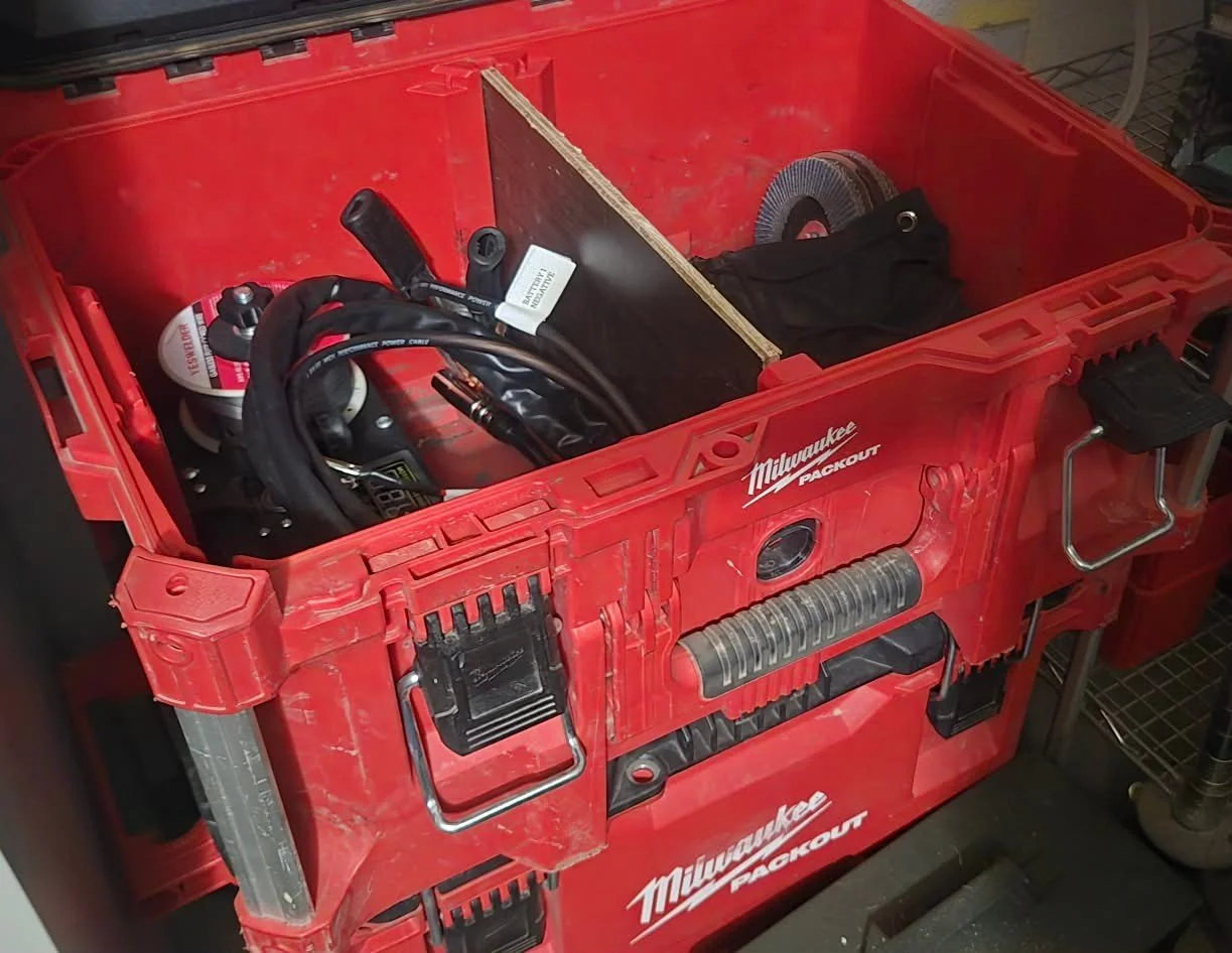 Red Milwaukee Packout toolbox with tools and equipment inside, including a grinder, a black fabric item, and cables.