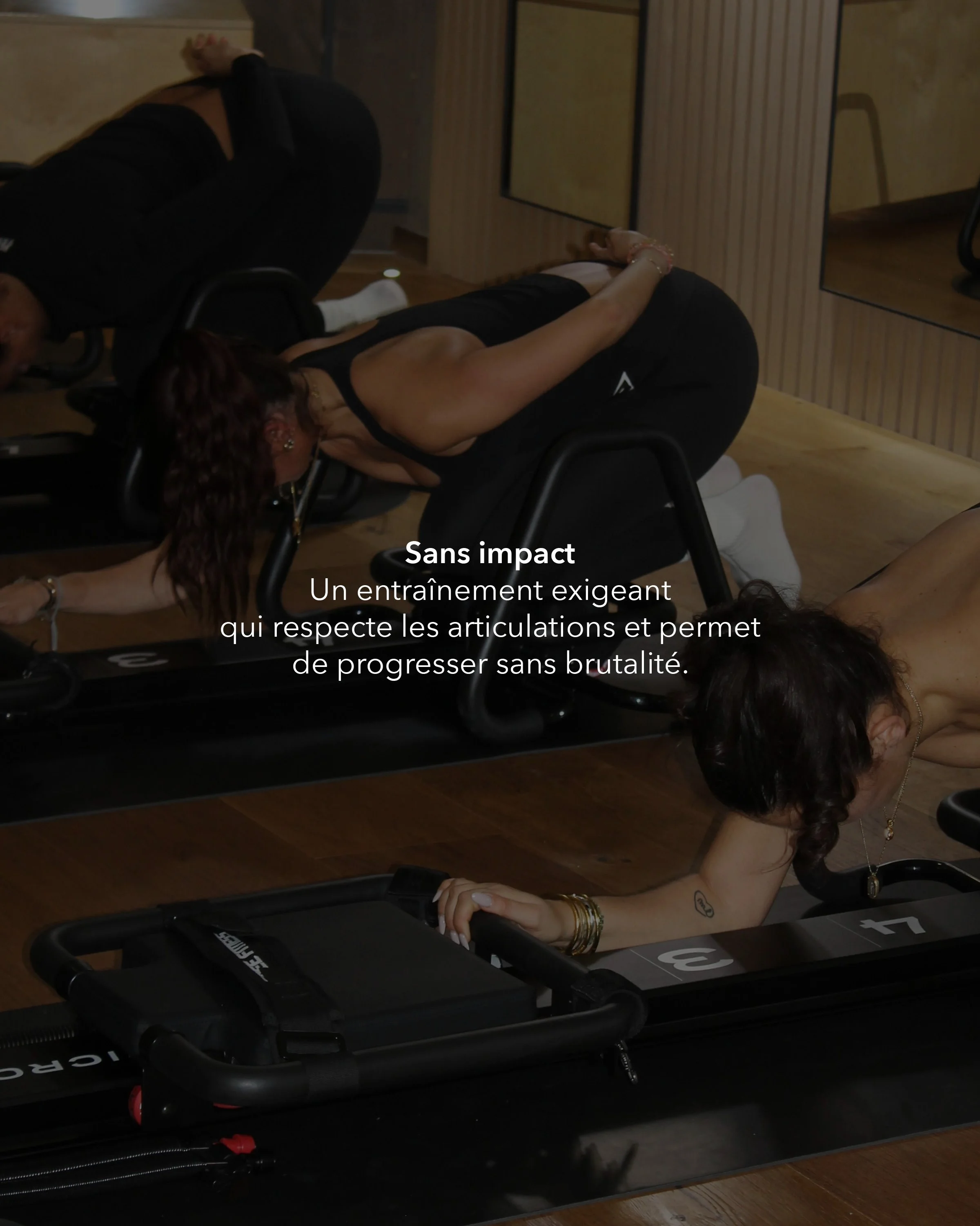 A woman with curly hair performing a stretch on a treadmill in a gym, with her body bent forward and her hands on the ground. The treadmill is black with white markings, and the background features wooden wall panels.