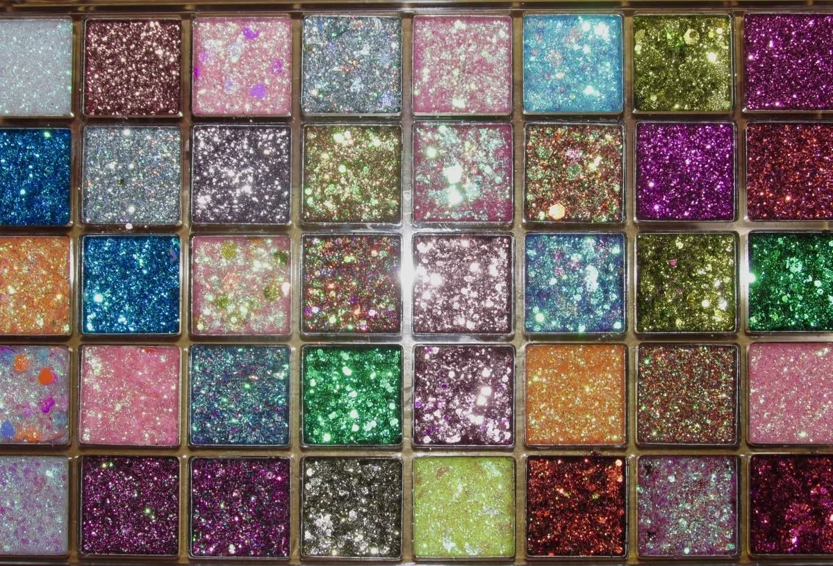 A collection of small, colorful, glittery square containers with various shades and sparkles, arranged in a grid pattern.