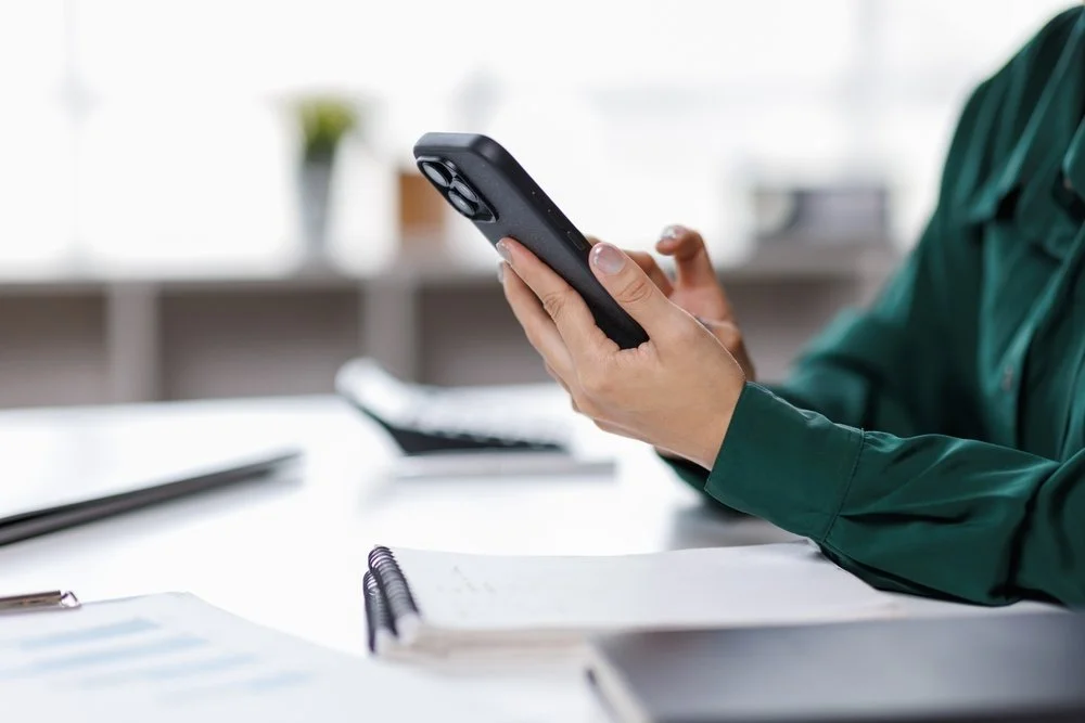Person in a green shirt holding a smartphone in an office setting.