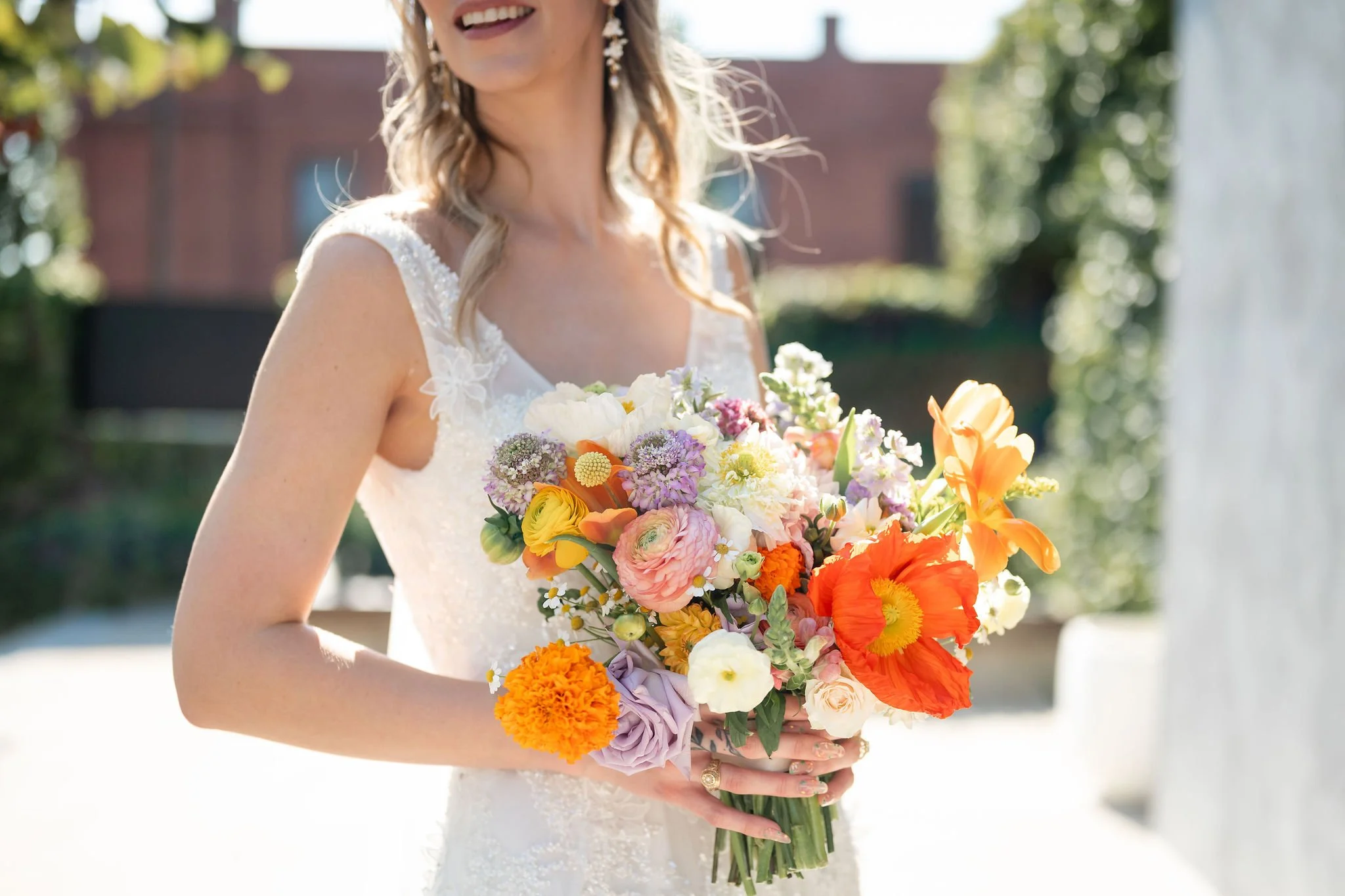 A woman in a wedding dress holding a bouquet of colorful flowers outdoors on a sunny day.