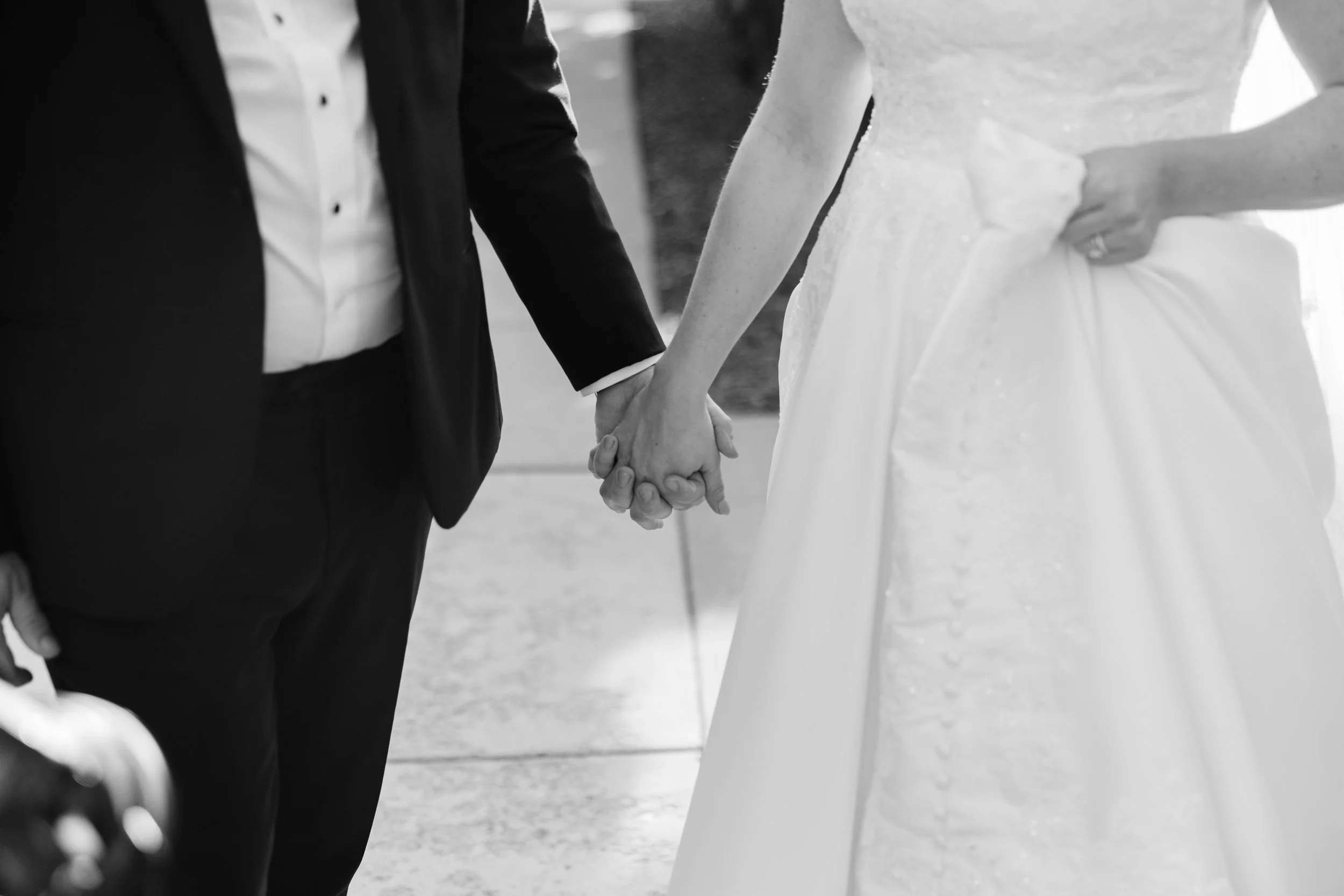 A close-up of a bride and groom holding hands during their wedding, with the bride wearing a wedding dress and the groom in a dark suit.