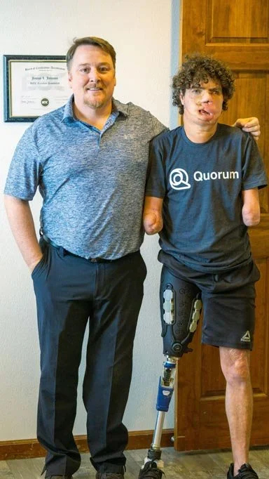 Damian, a One Leg At A Time recipient, standing beside his prosthetist while wearing a custom lower limb prosthesis. Learn more about Damian’s story and prosthetic care.
