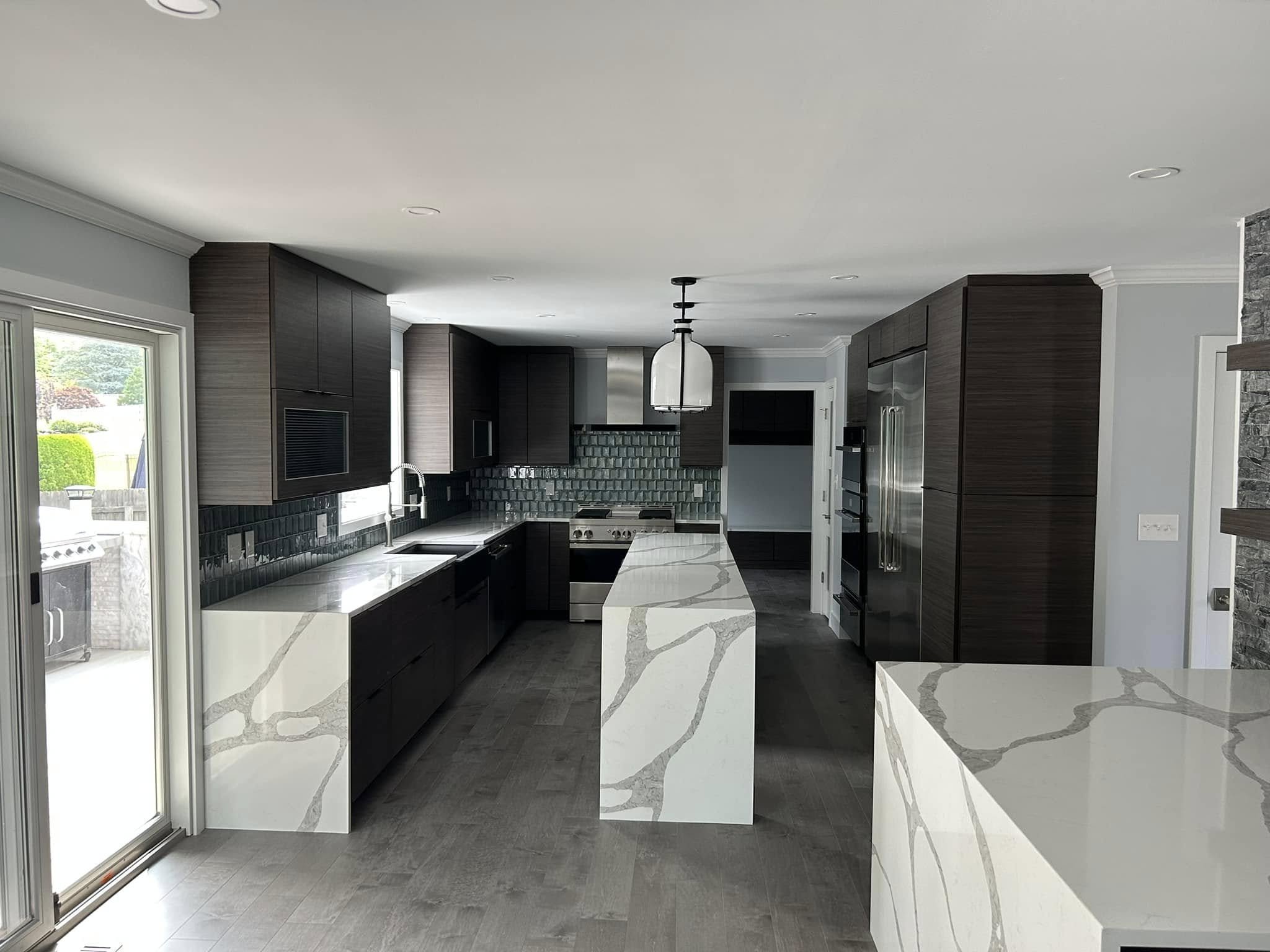 Modern kitchen with dark wood cabinets, black tiled backsplash, marble countertops, and stainless steel appliances, with large window and sliding glass door.