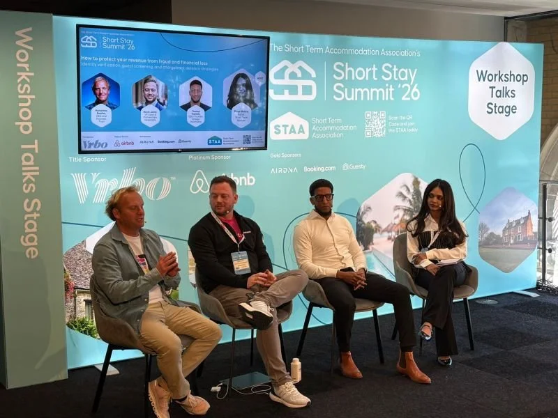 Panel discussion at the Short Stay Summit '26 on Workshop Talks Stage, featuring four individuals seated on a stage with a large backdrop displaying event information and sponsor logos.