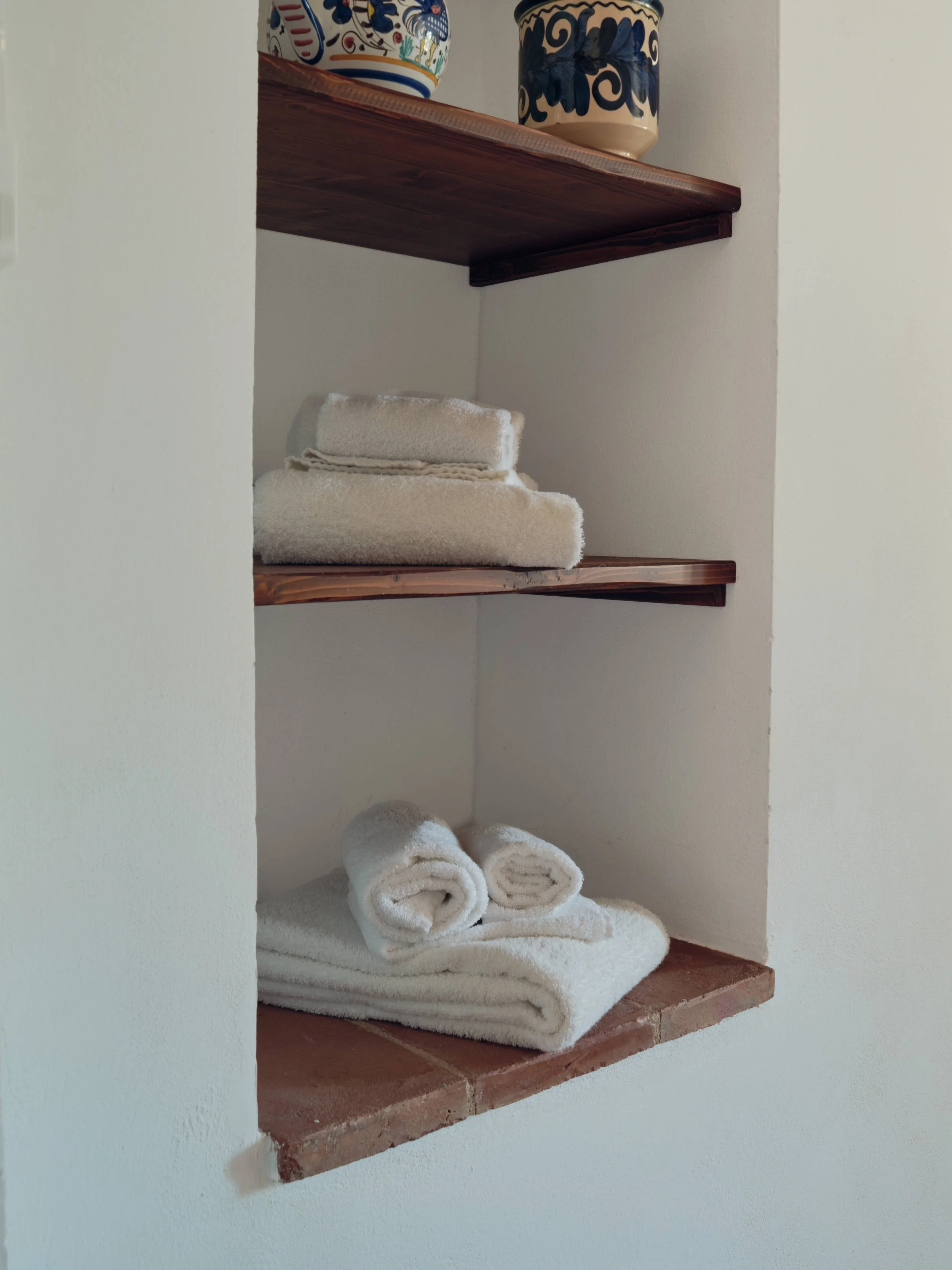 A wall shelf with decorative ceramic vases on top and neatly folded towels on the bottom shelf.