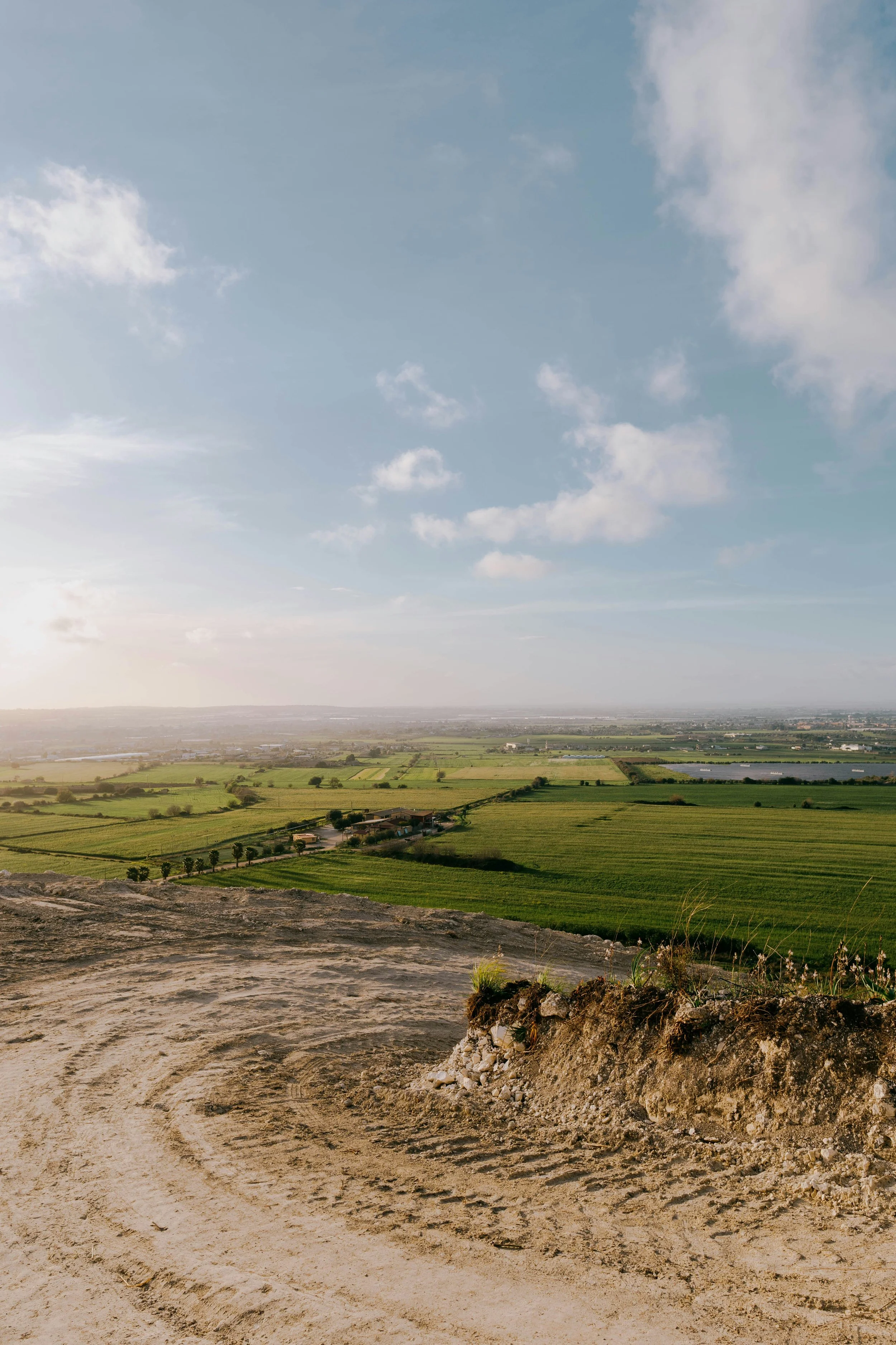 View of a rural landscape with green fields, scattered houses, and a distant horizon under a partly cloudy sky.
