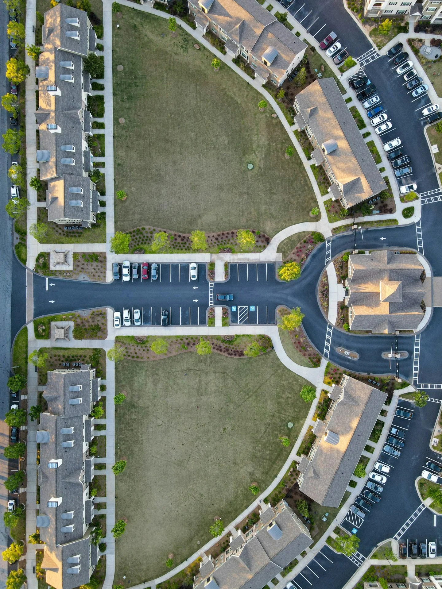 Aerial view of a residential apartment complex with a large grassy central area, surrounded by parking lots, walkways, and apartment buildings.
